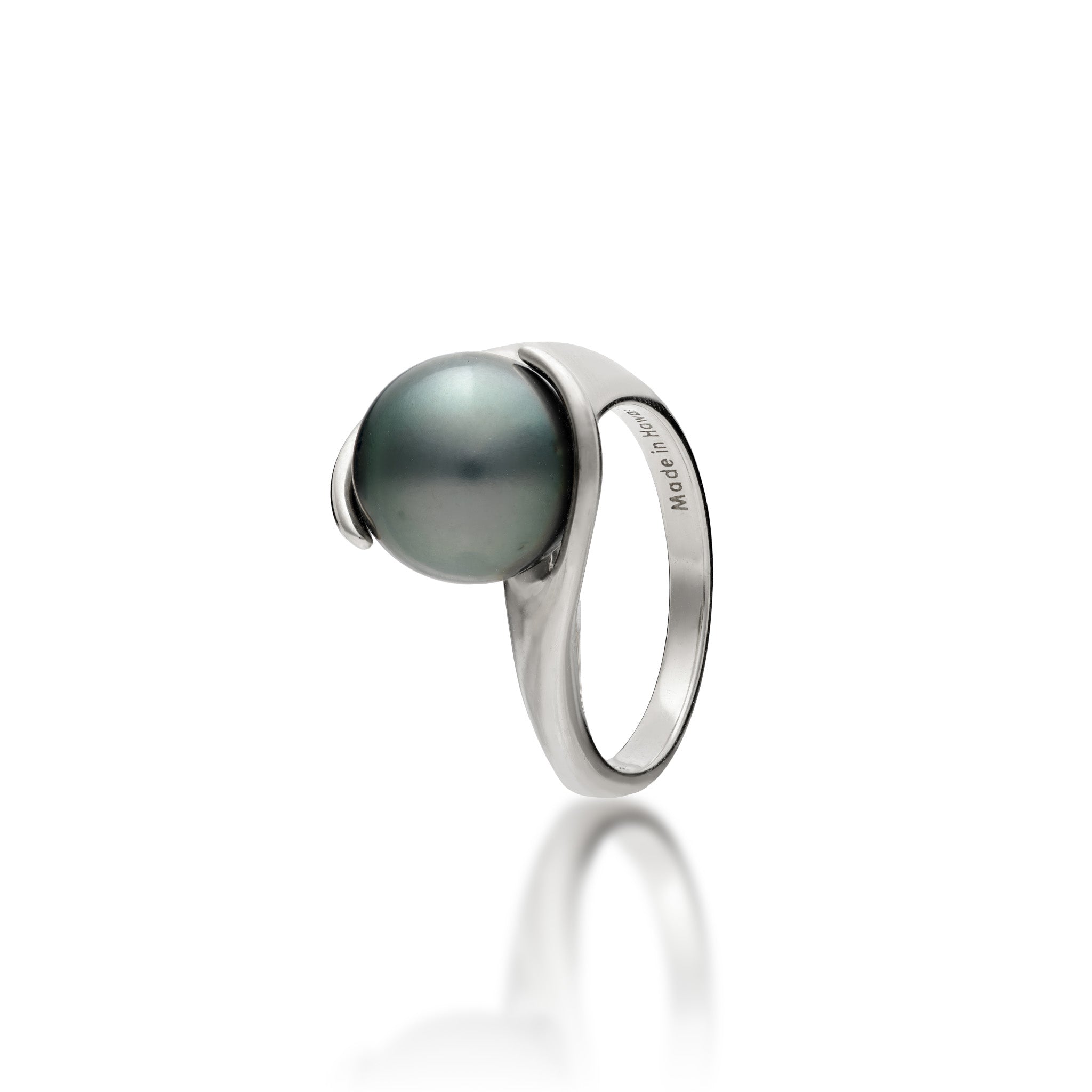 A simple 14k white gold ring featuring a Tahitian black pearl with curved gold wrapped around each side, shown on a clean white background with a soft reflection below. The inside of the band is engraved with 'Made in Hawaii'.