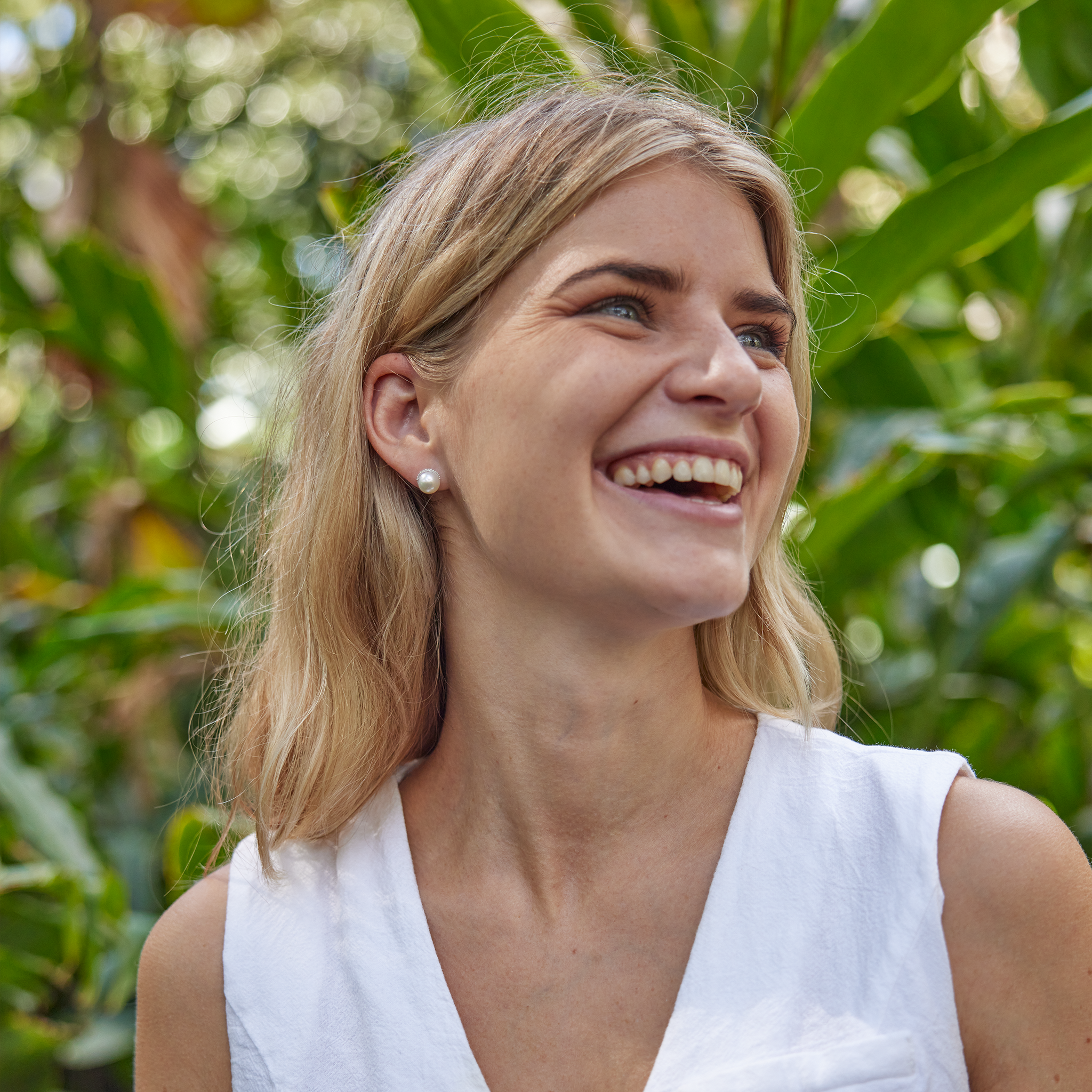 Woman in garden laughing and wearing Halo Akoya White Pearl Earrings in White Gold with Diamonds - 8-8.5mm
