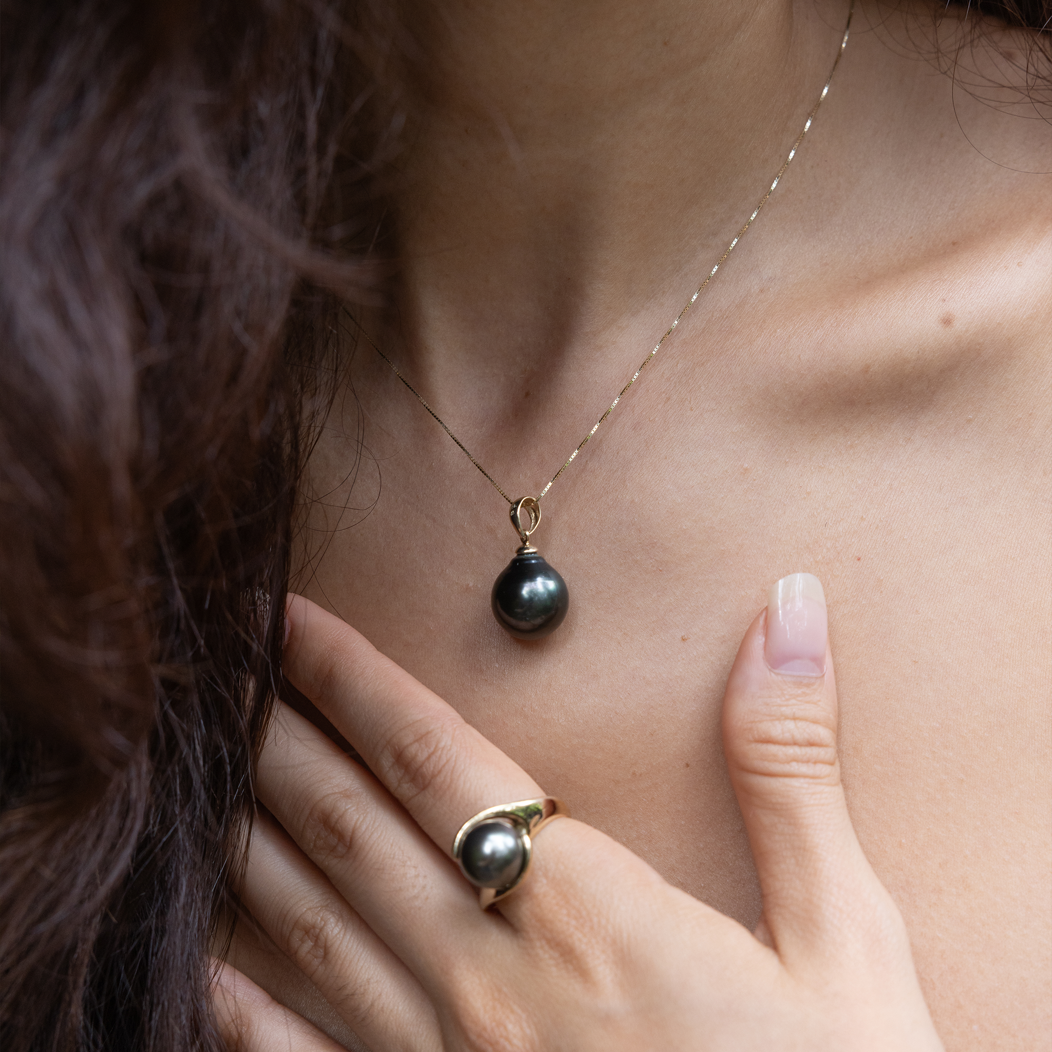 Close-up of a woman wearing a drop-shape Tahitian black pearl pendant and a matching ring.