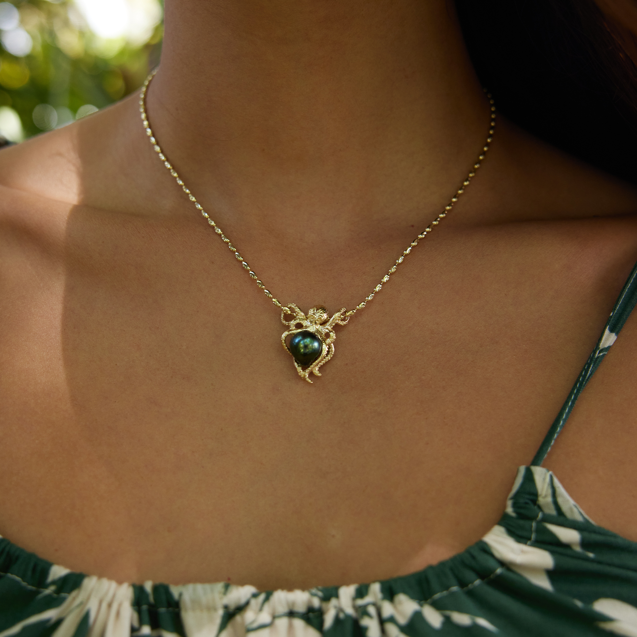Close-up of a person wearing a Octopus Tahitian black pearl pendant in 14k yellow gold.