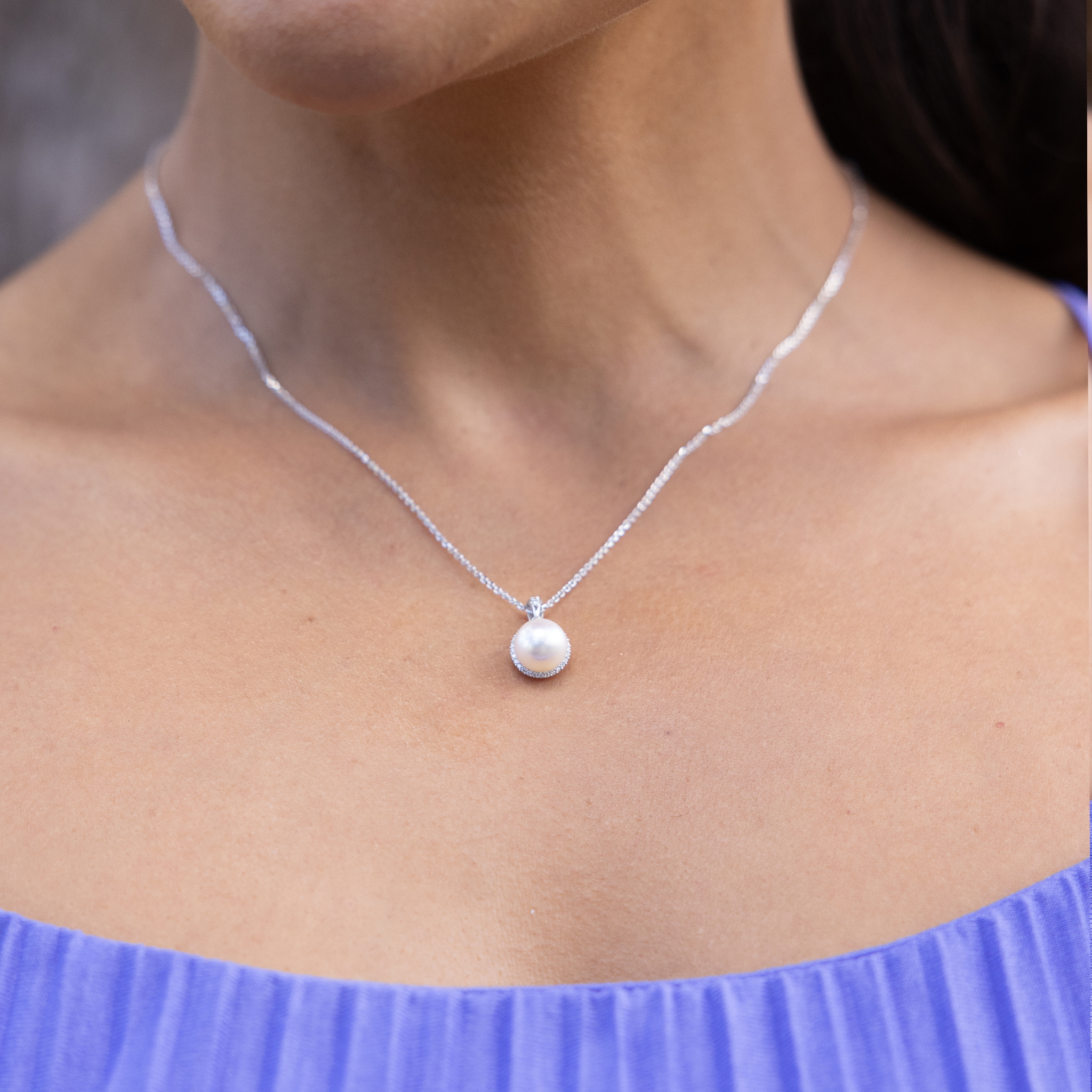 Close-up of a person wearing a diamond. halo, Akoya white pearl pendant in white gold.