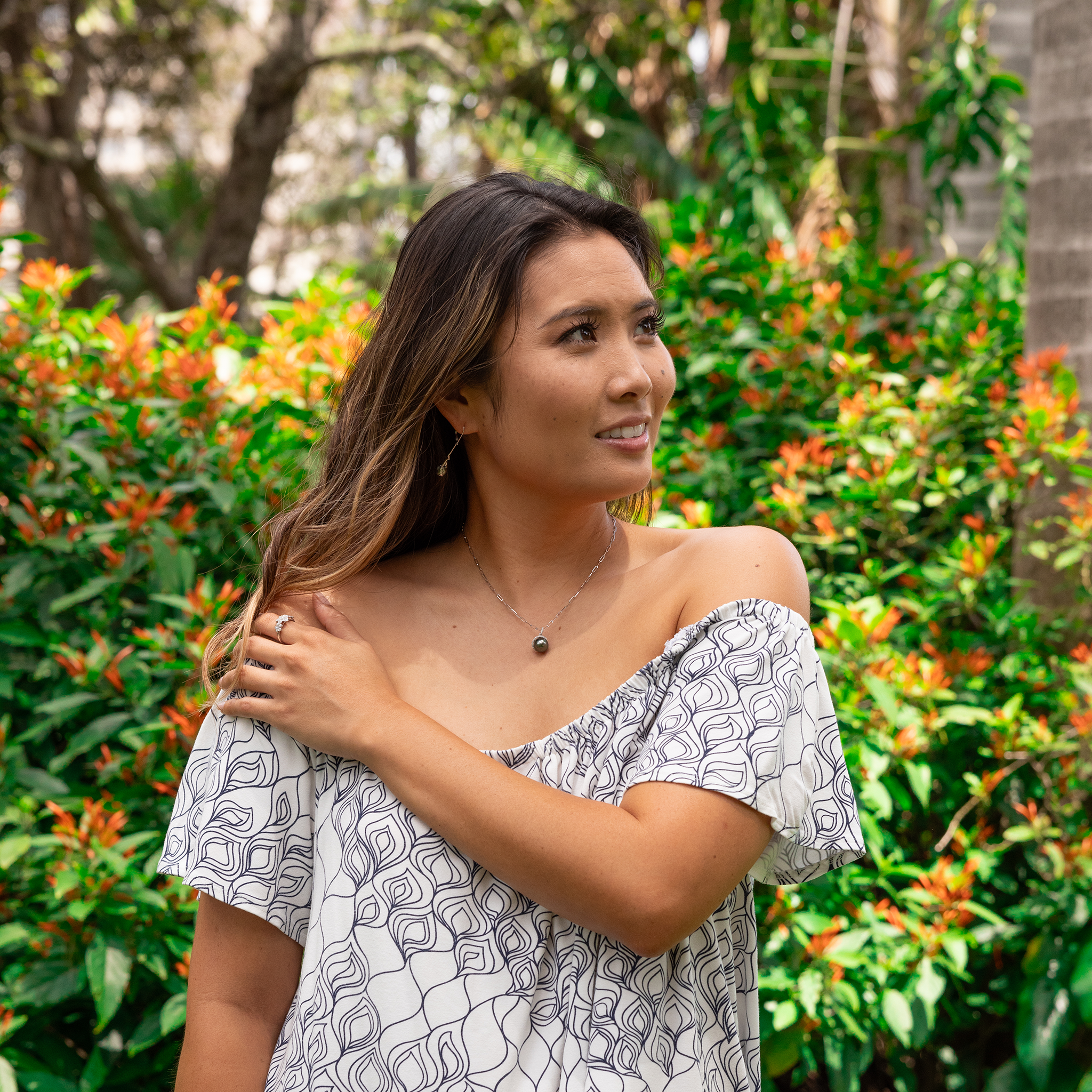 Woman ina flower garden wearing a diamond halo Tahitian black pearl pendant on a white gold paperclip chain