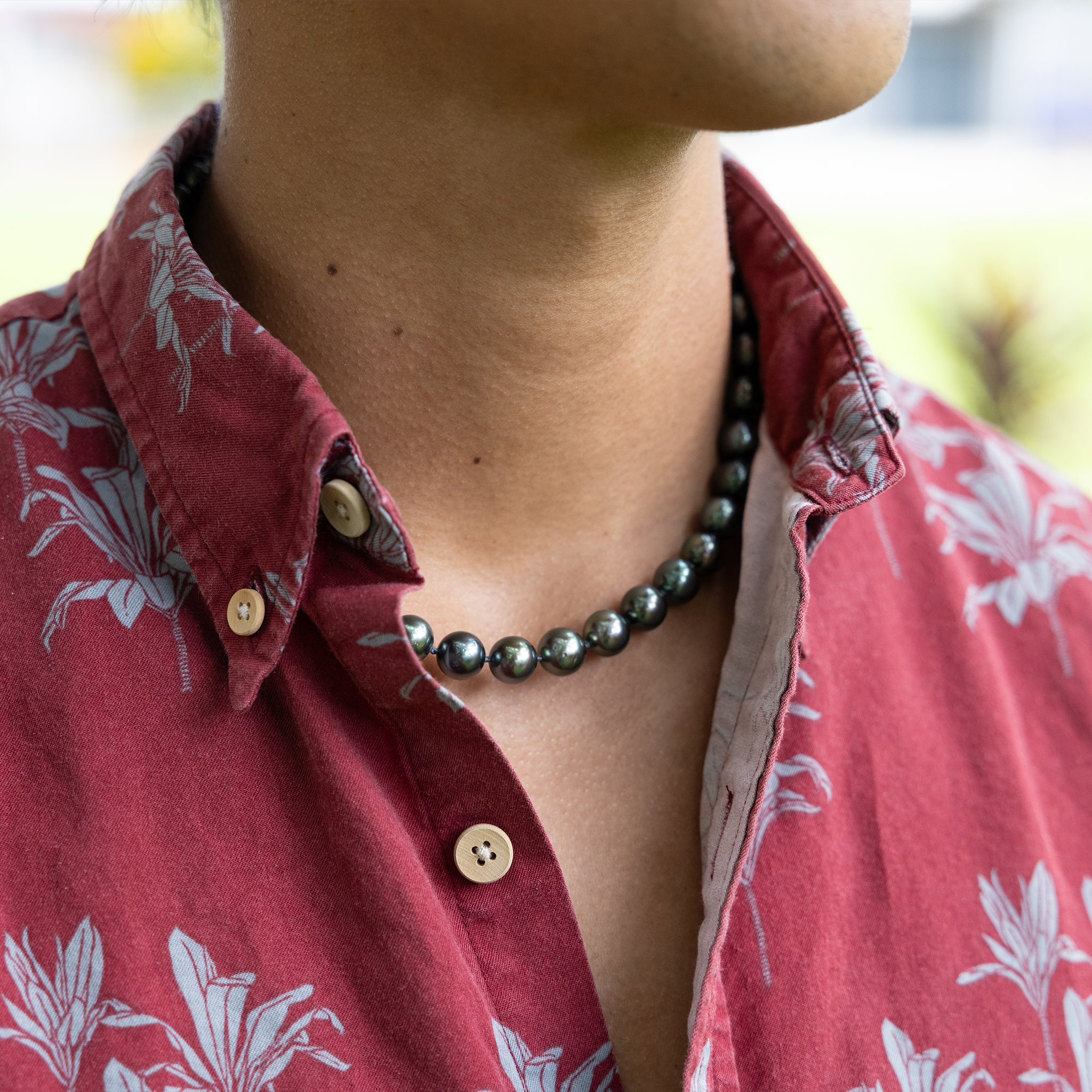 Close up of a man in a red shirt wearing a Tahitian black pearl strand