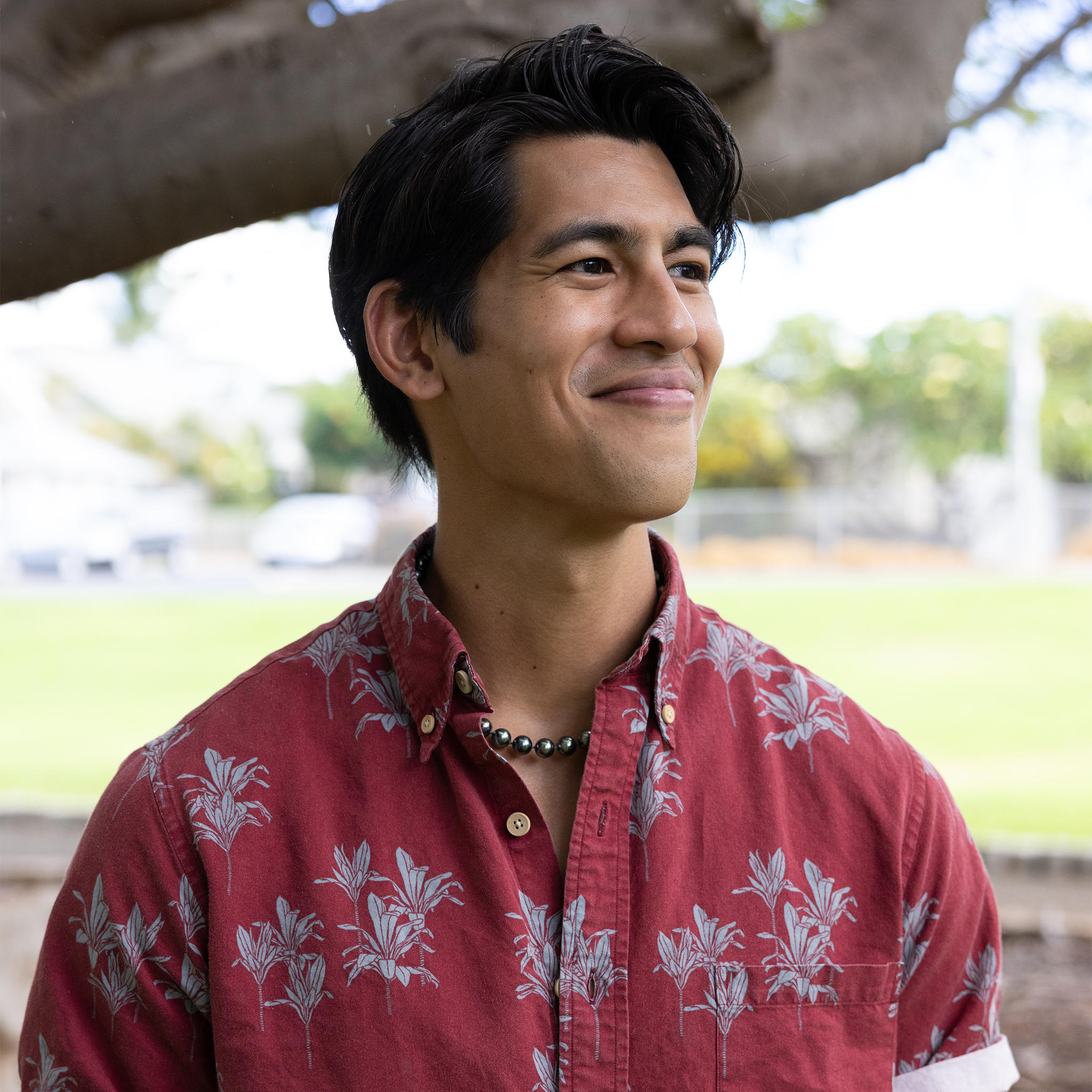 Man in a red shirt wearing a Tahitian black pearl strand with a blurry green background