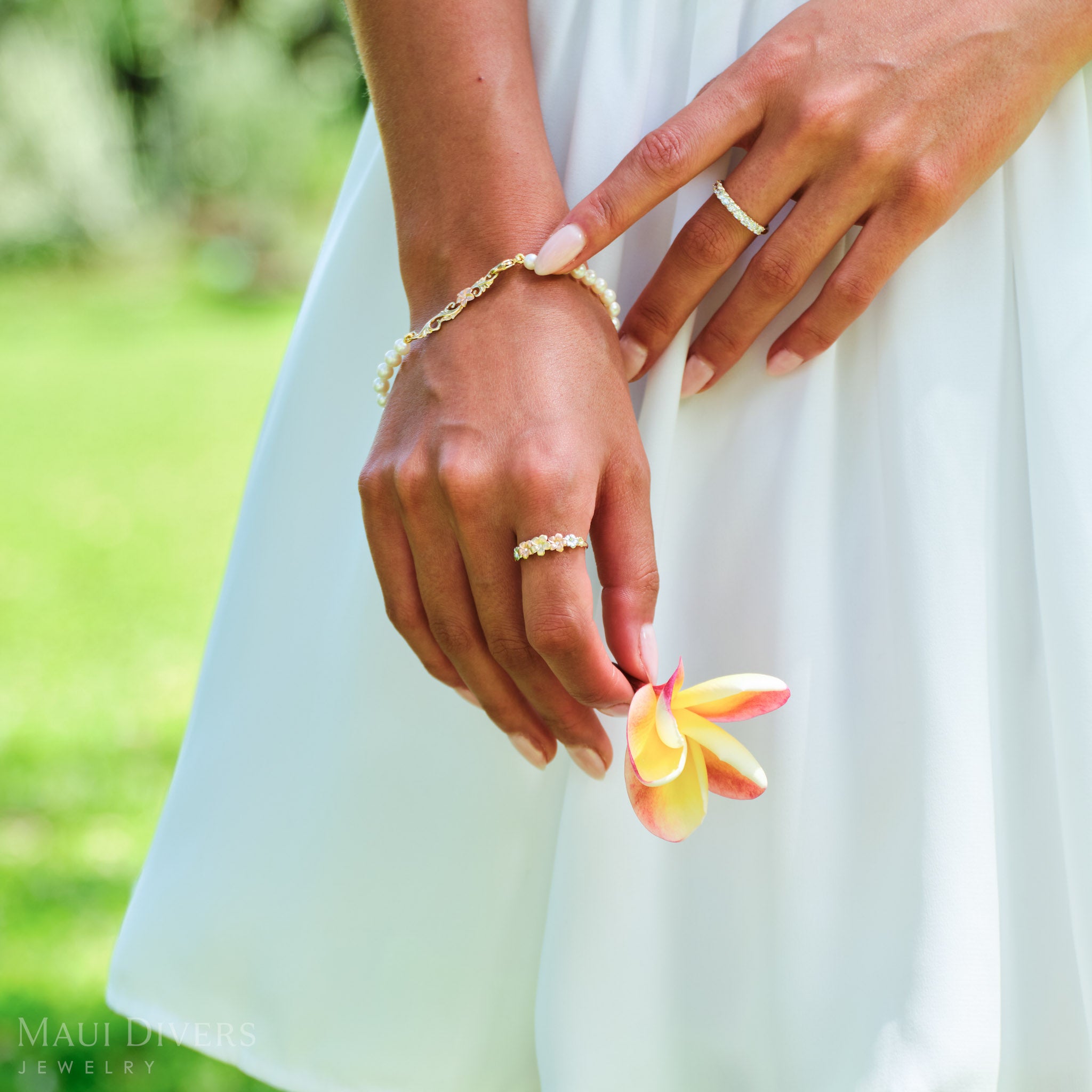 Close-up of a hand holding a plumeria flower wearing a Plumeria Ring in Tri Color Gold with Diamonds