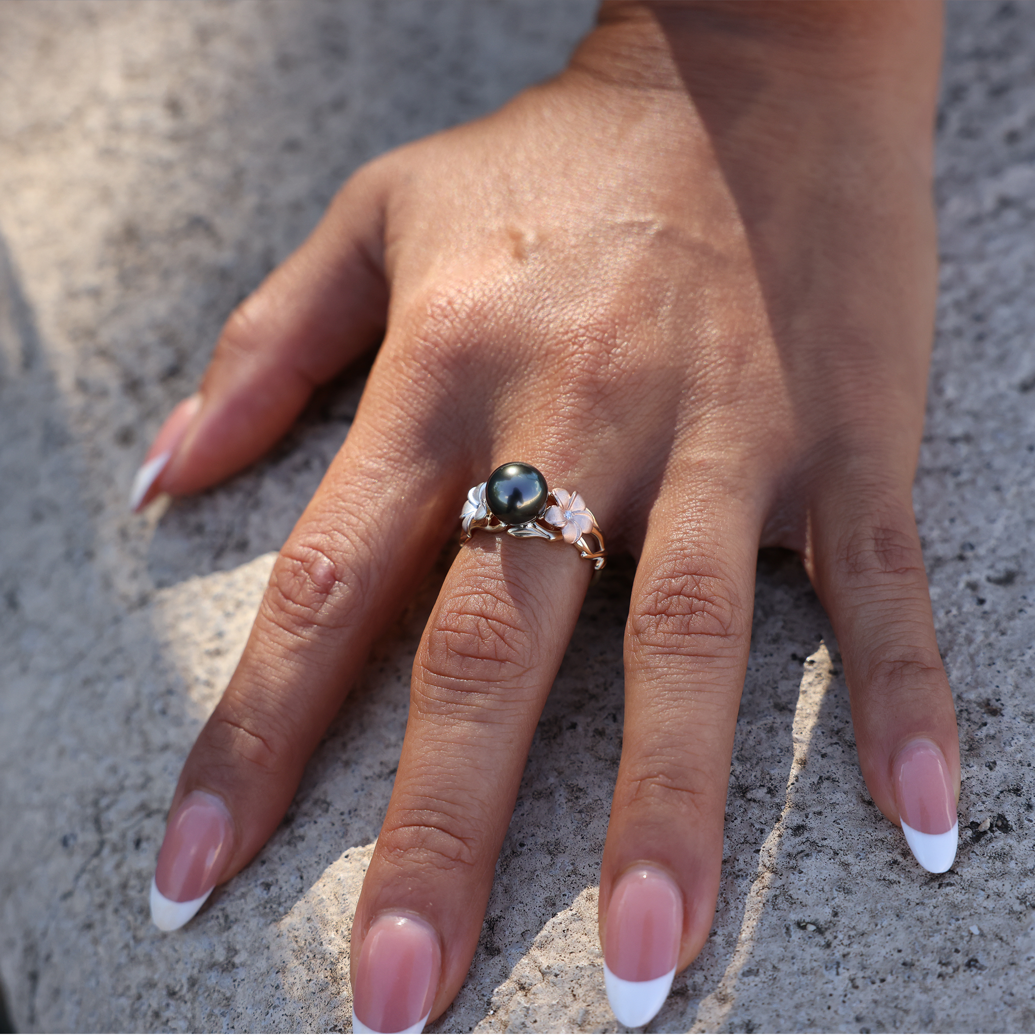 Maui Divers Jewelry Pearls in Bloom Plumeria Tahitian Black Pearl Ring in Tri Color Gold with Diamonds on Hand touching cement wall