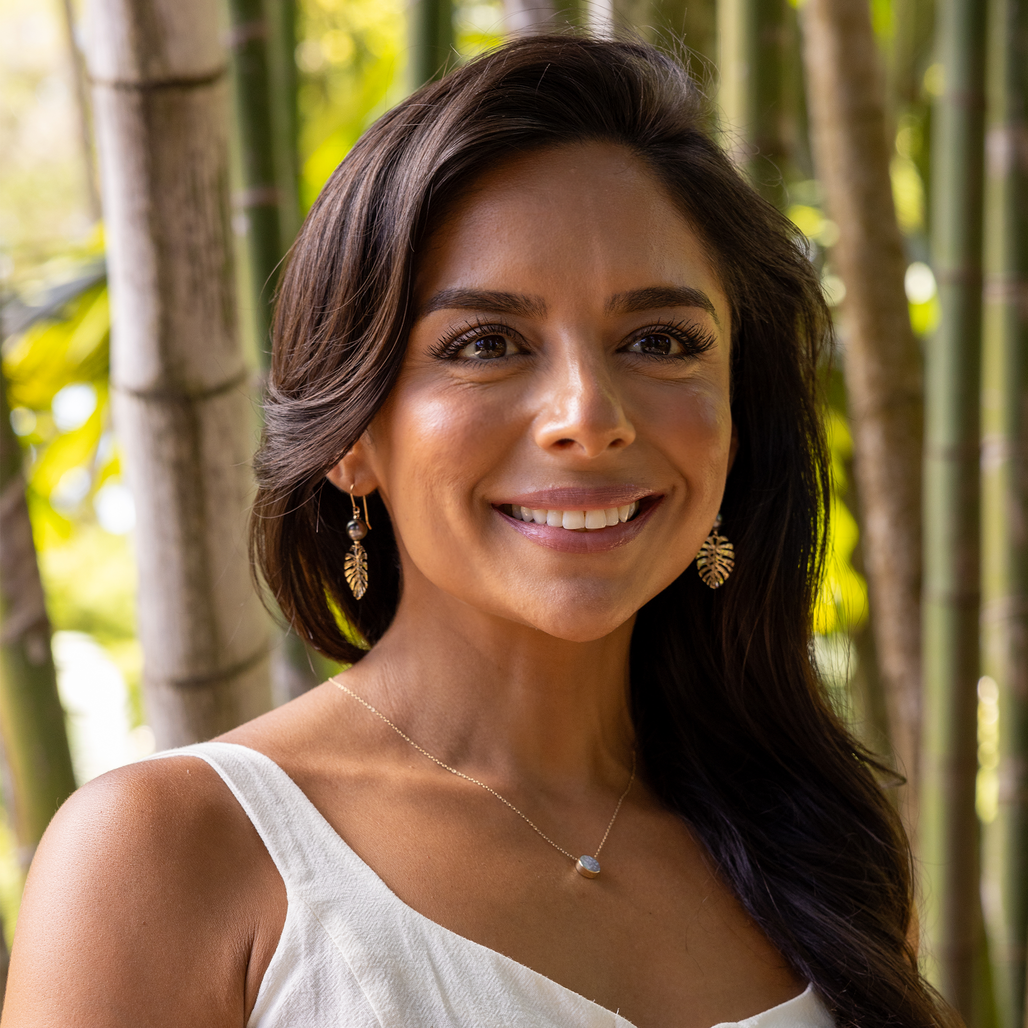 Woman in a bamboo garden wearing 23mm Monstera Tahitian Black Pearl Earrings in Gold