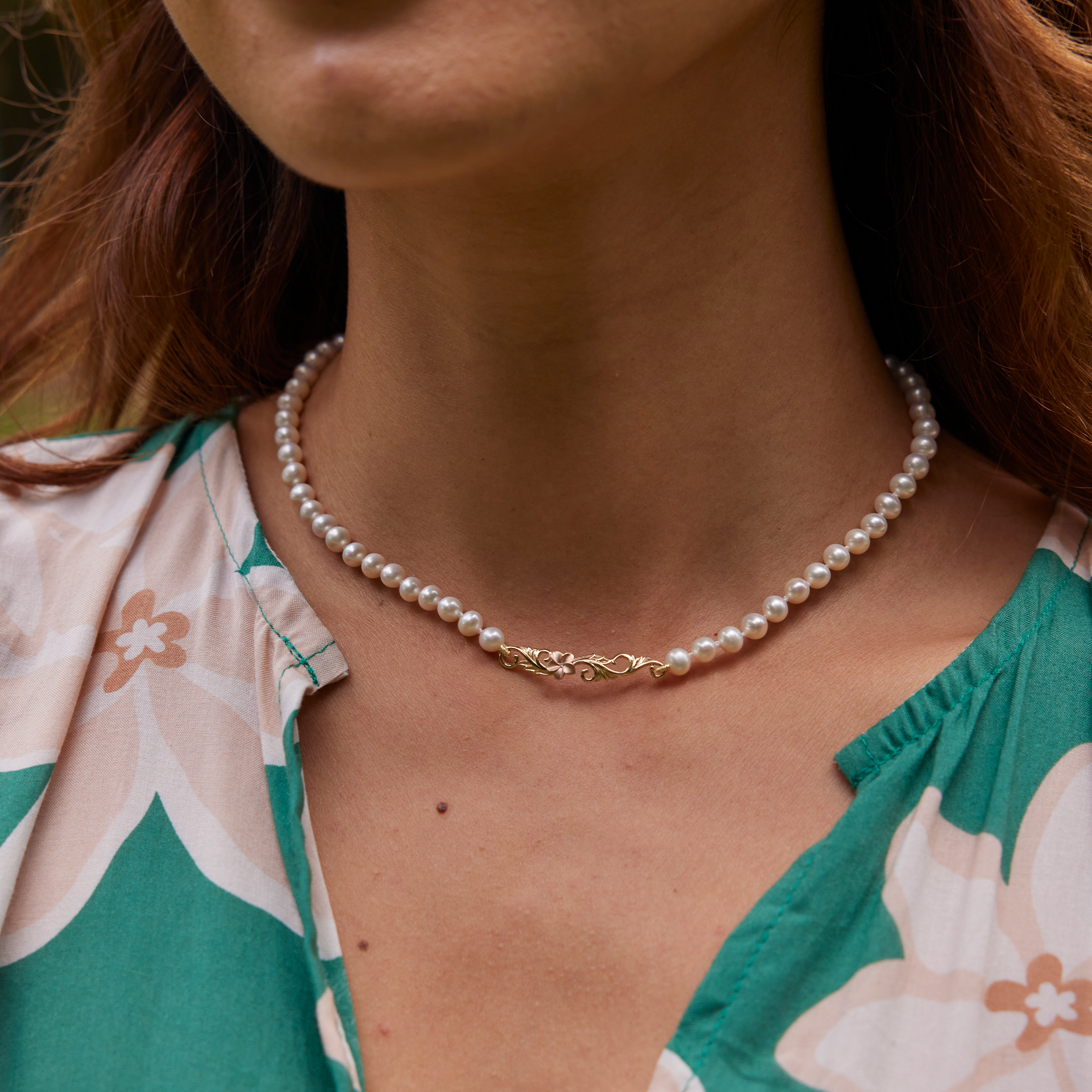 Close up of a person wearing the Hawaiian Heirloom Plumeria Freshwater White Pearl Necklace