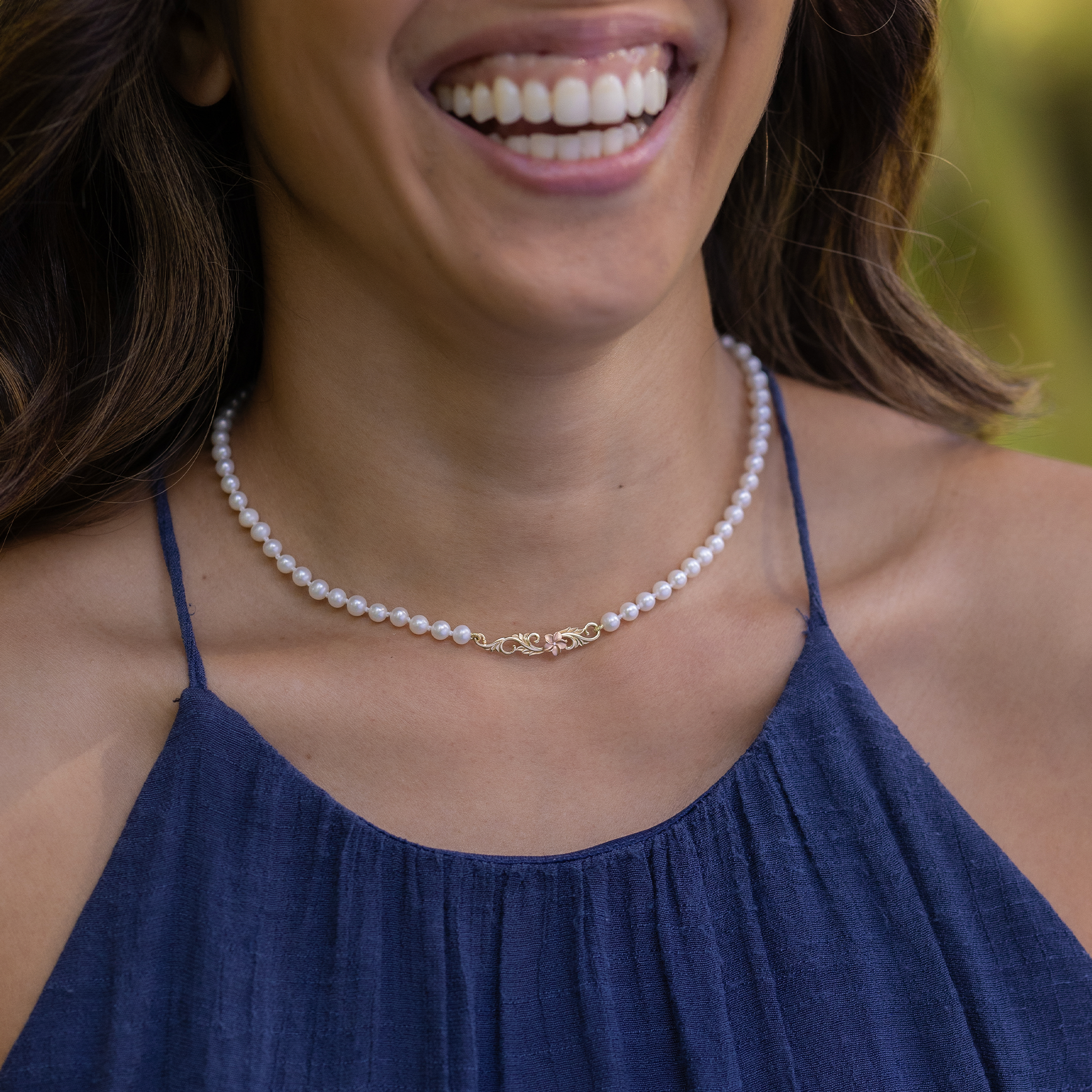 Close up of a woman wearing the Hawaiian Heirloom Plumeria Freshwater White Pearl Necklace