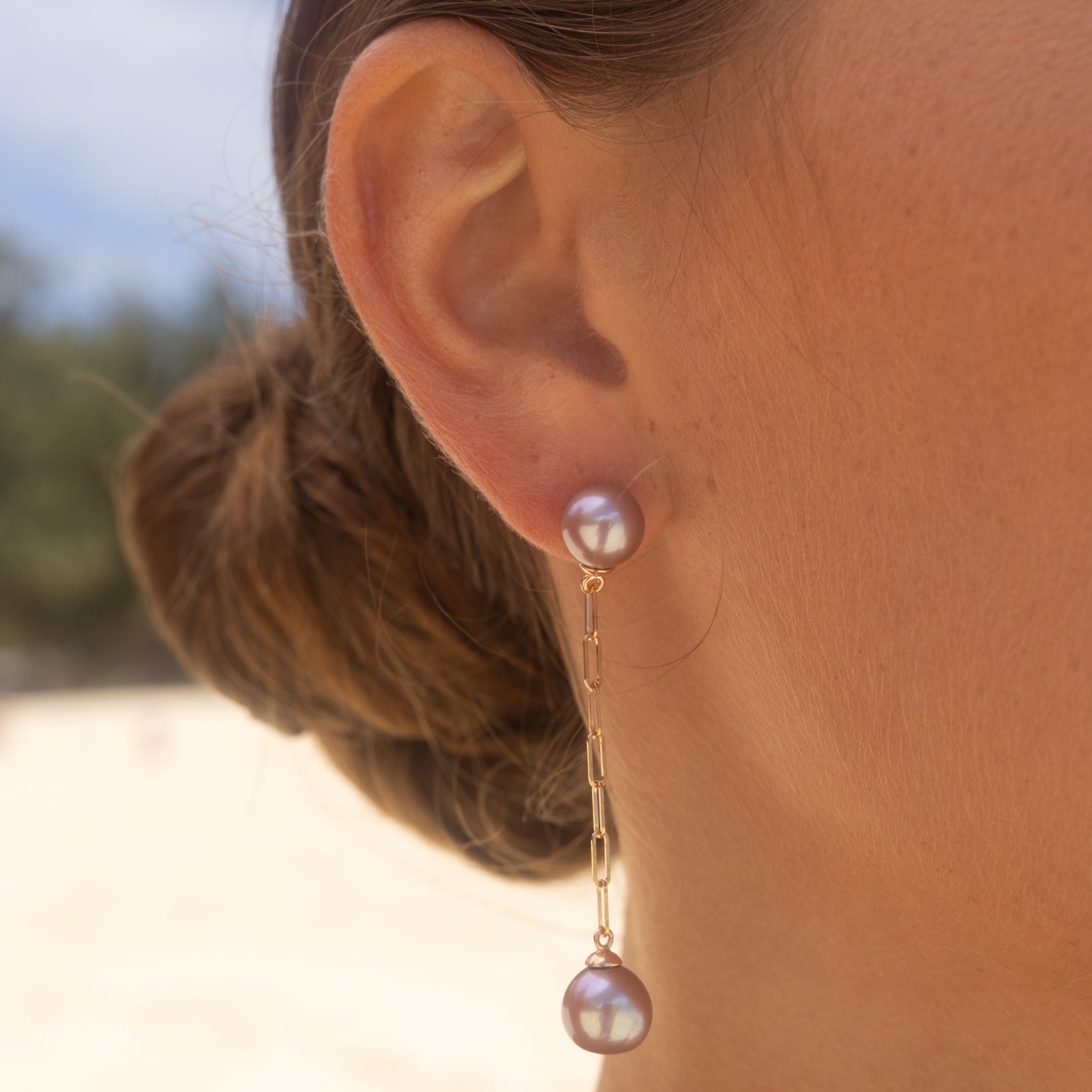 Close-up of a person wearing Freshwater Ultraviolet Pearl Paperclip Chain Earrings in Rose Gold outdoors