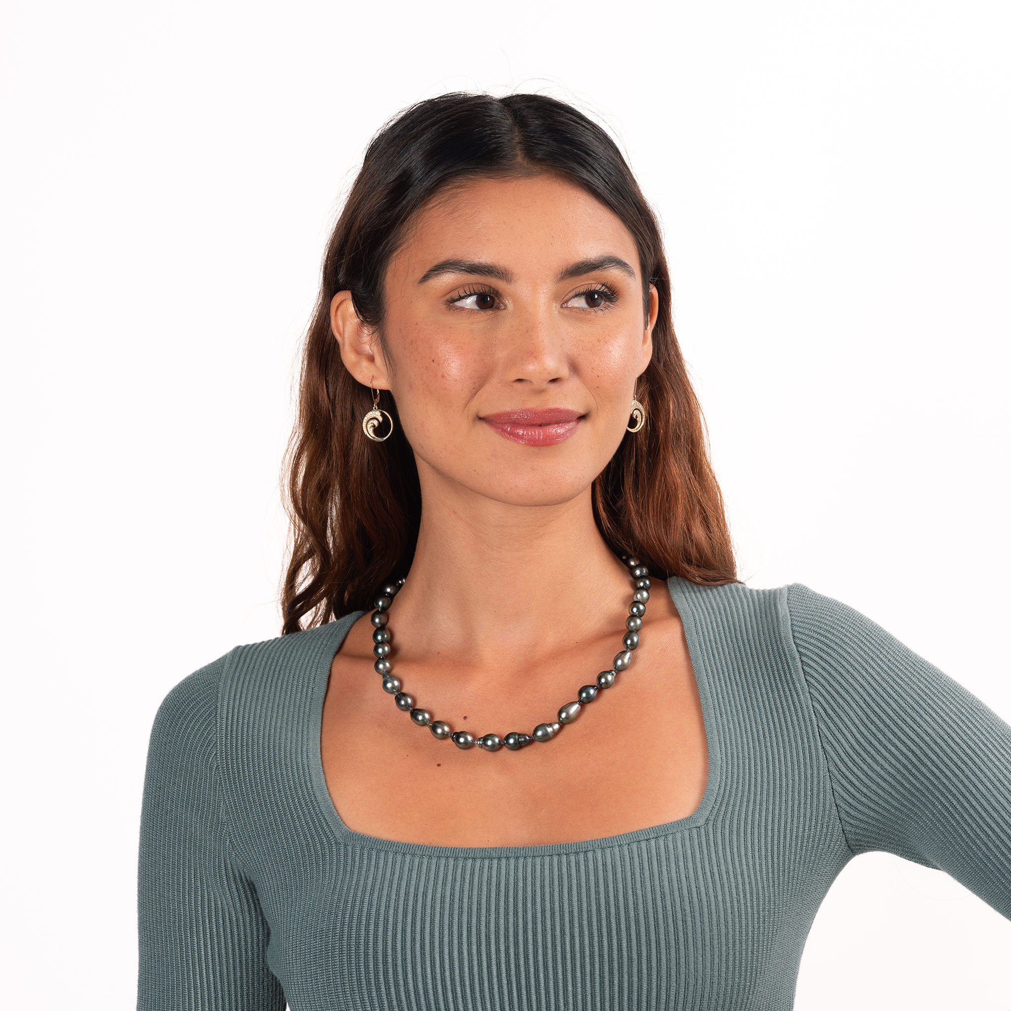 Woman in a teal shirt wearing a baroque Tahitian black pearl strand and diamond wave earrings with a white backdrop