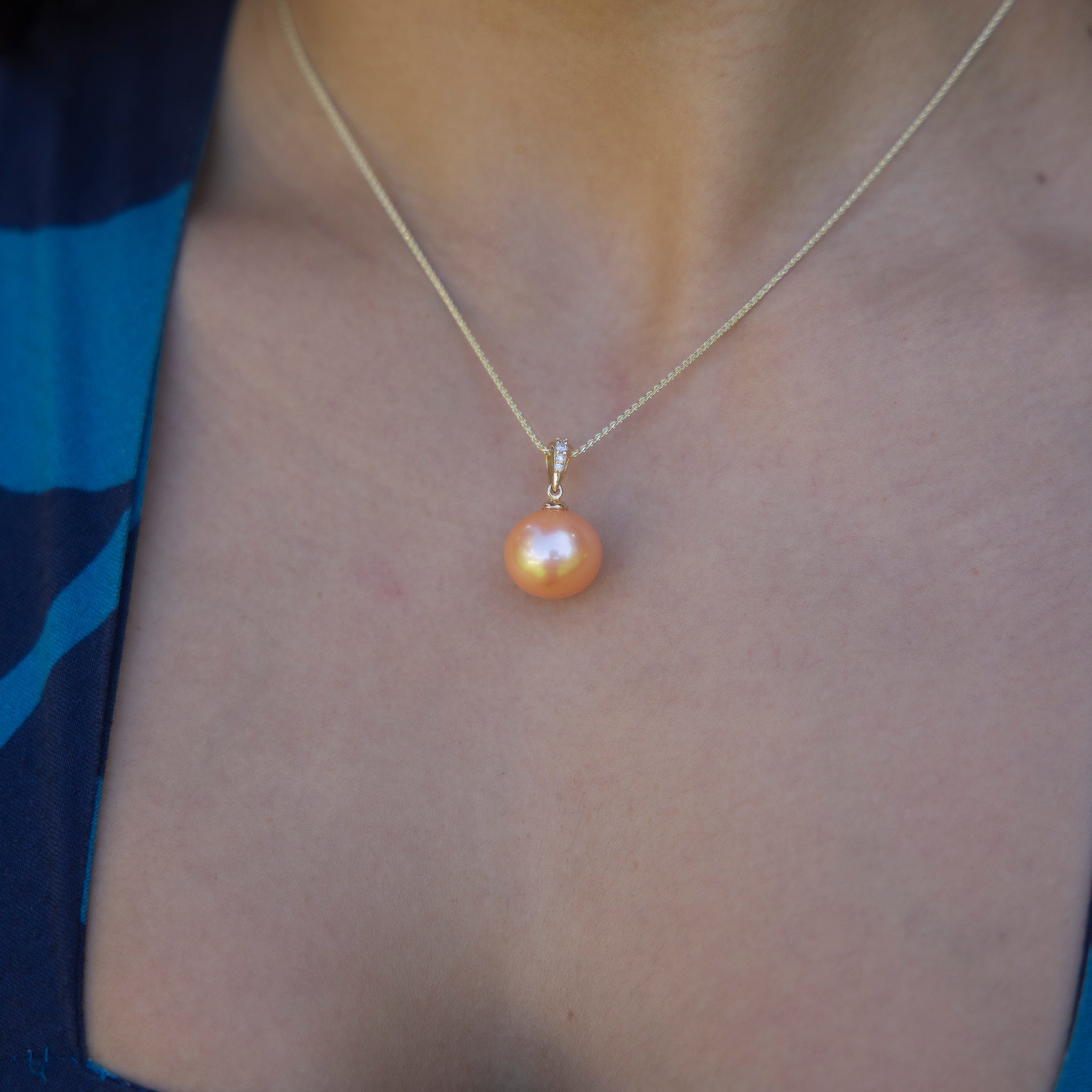 Person wearing a peach freshwater pearl pendant with diamond accents