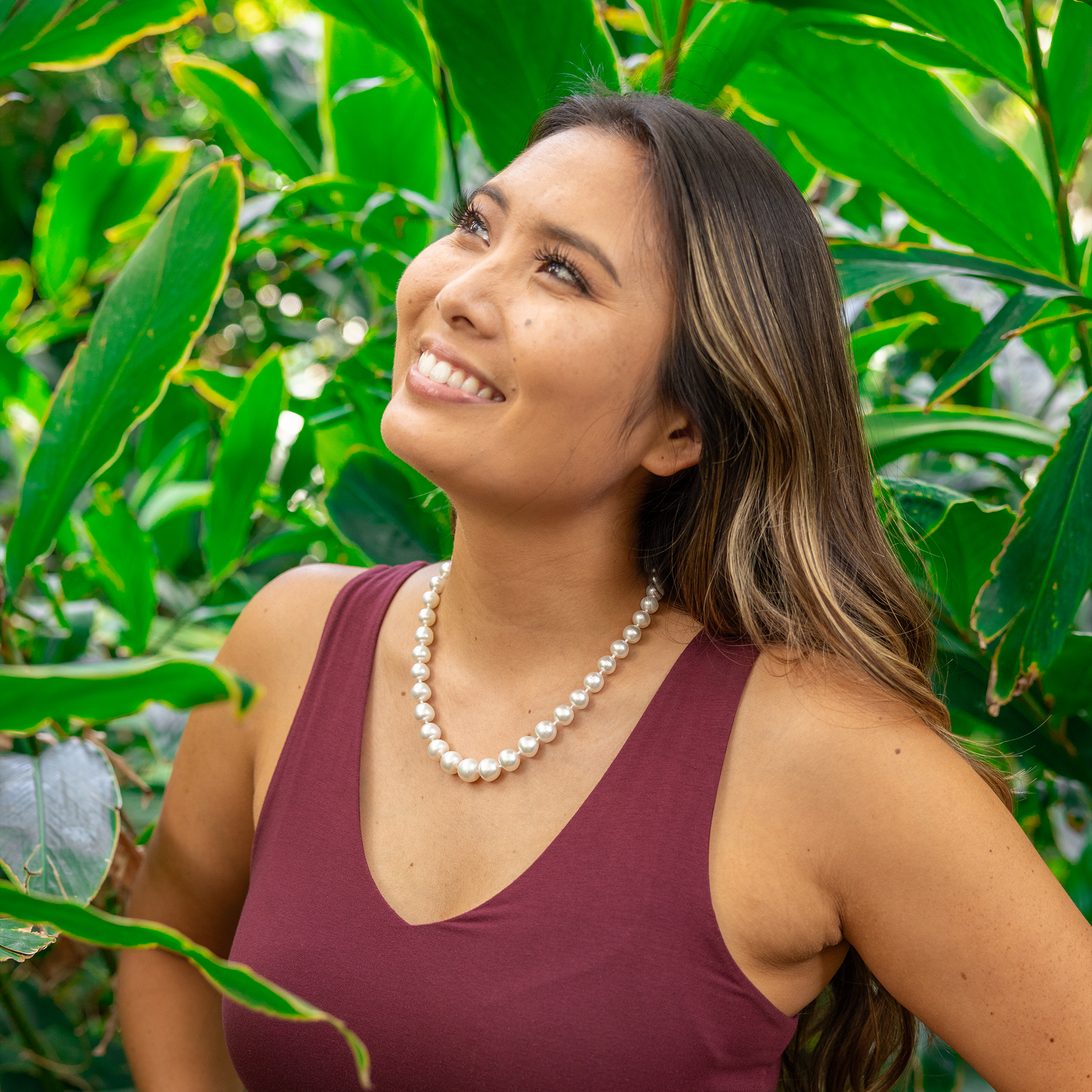 Woman in a tropical garden wearing an 18-19" 9-10mm South Sea White Pearl Strand with Magnetic Clasp in Gold