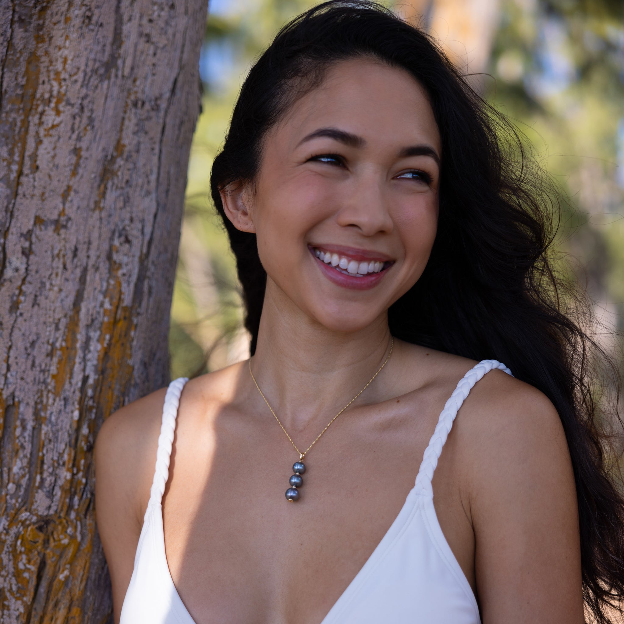 Smiling woman leaning on a tree and wearing a Three Stacked 10-11mm Tahitian Black Pearl Pendant in Gold