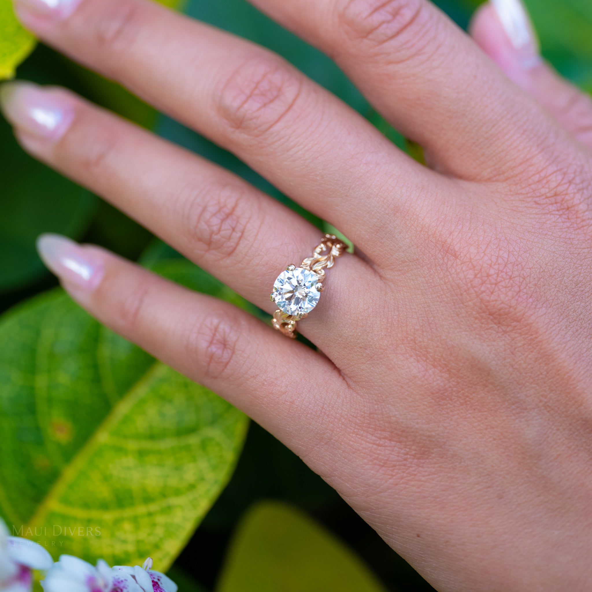 Hand wearing a 14k yellow gold Living Heirloom Engagement ring with a solitaire 2.02 carat lab grown diamond, set against a green leafy background