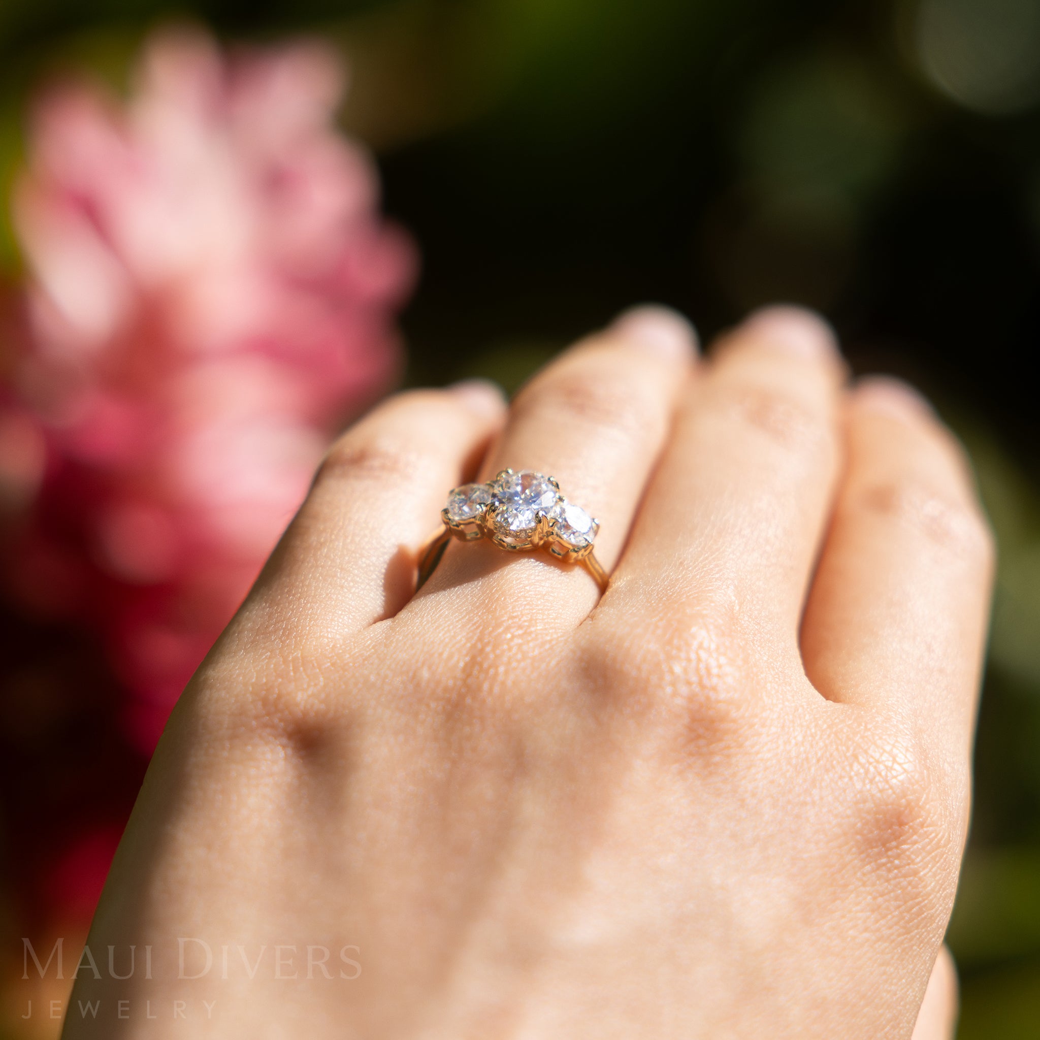 Hand wearing a lab-grown diamond ring with a blurred floral background