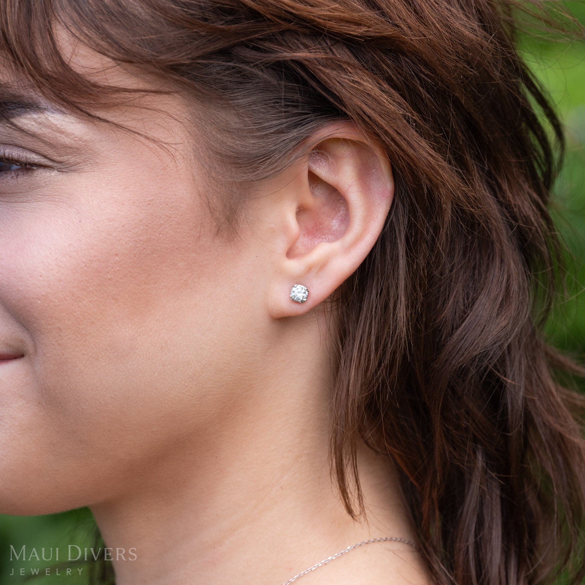 Close up on an womanʻs ear wearing a lab-grown diamond maile leaf stud earrings in 14k white gold
