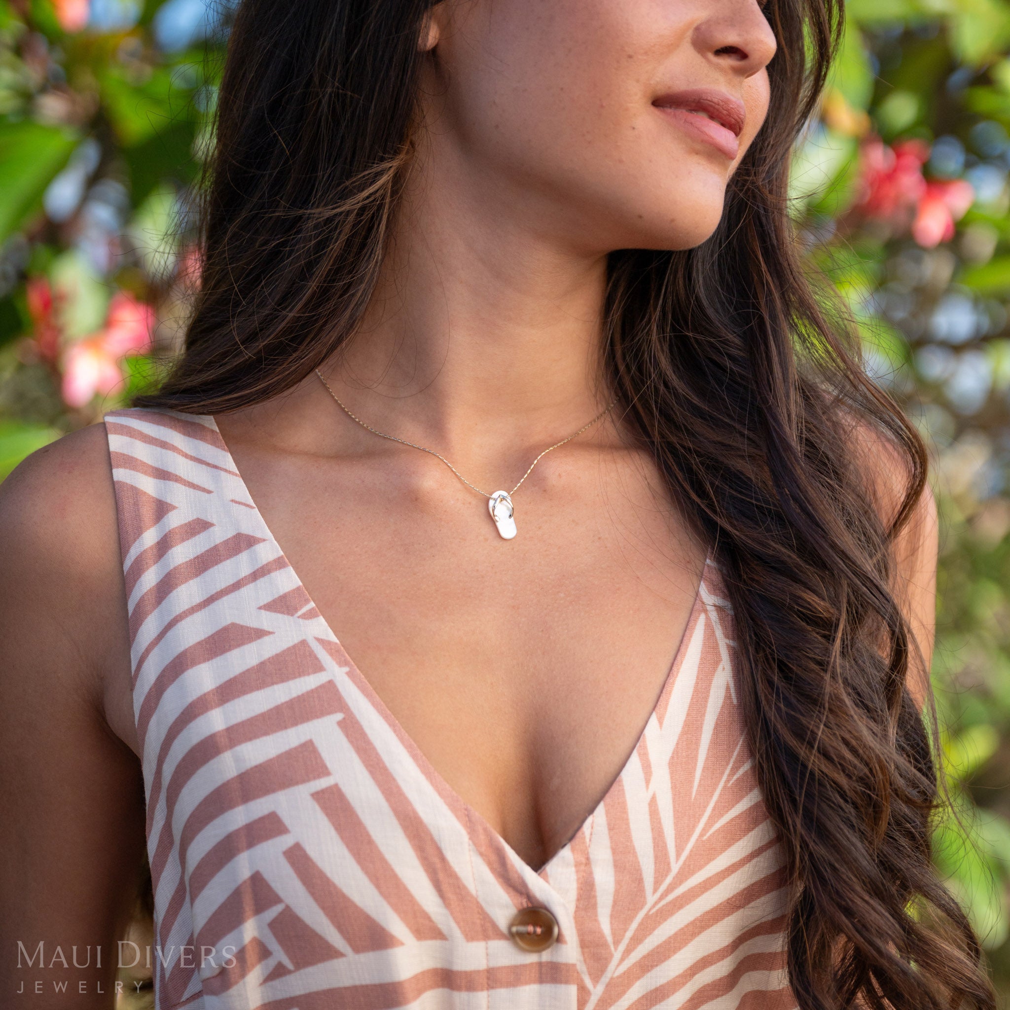 Woman with a neckline showing a White Mother of Pearl Slipper Pendant with 14k Gold details with a pink and green nature background.