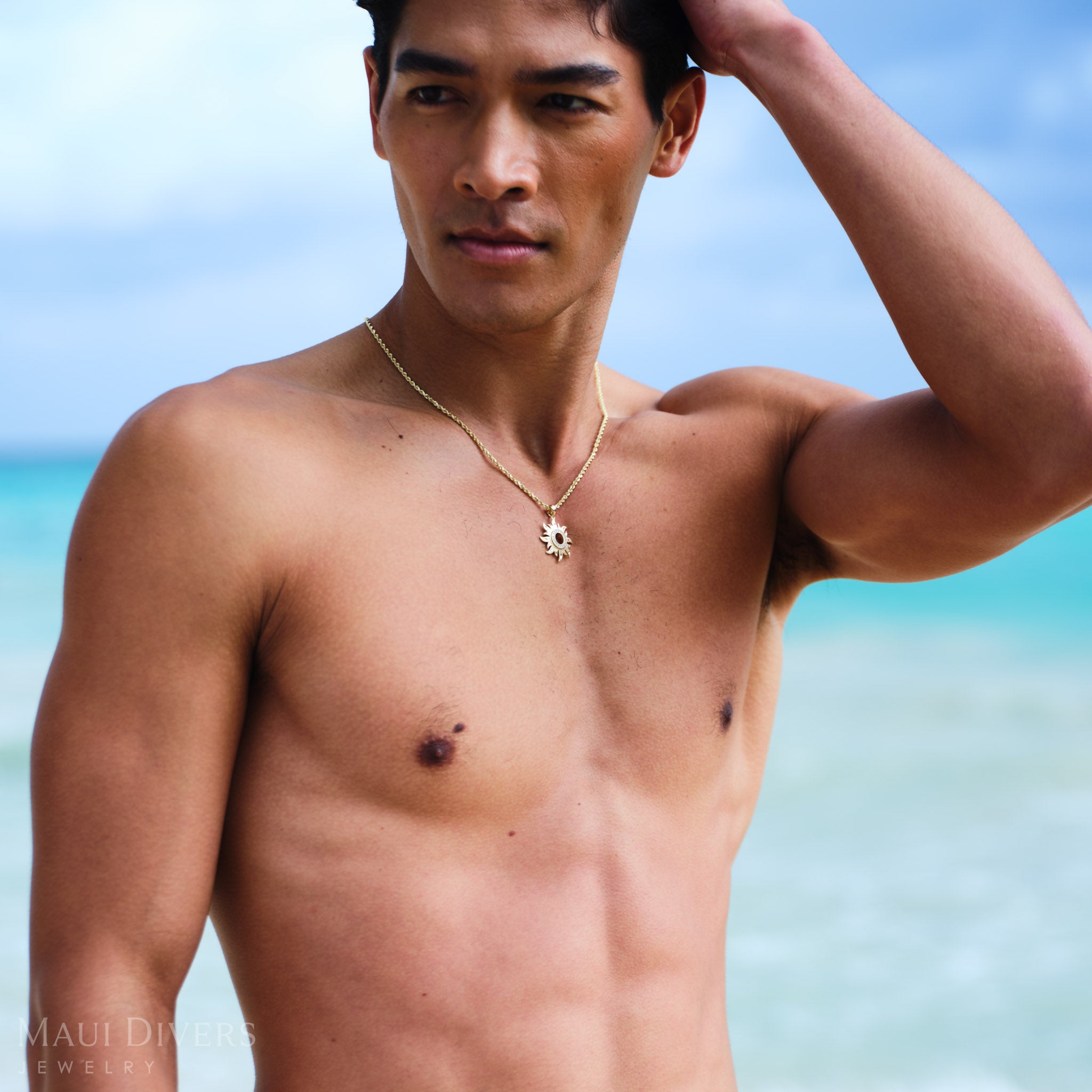 Man wearing a gold rope chain with a sun pendant against a beach background