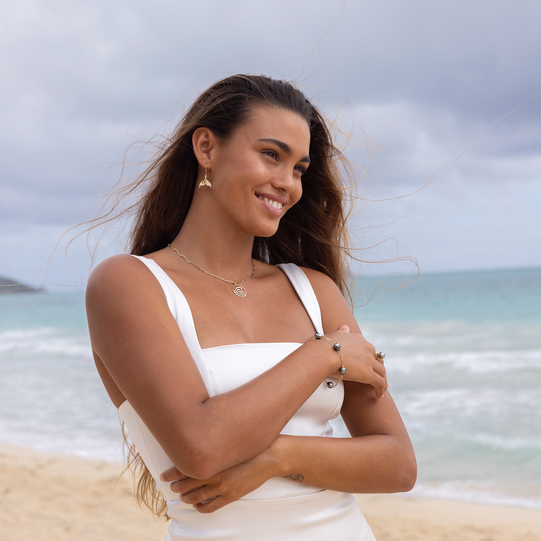 Woman on a beach wearing a white dress with a wave necklace on a paperclip chain