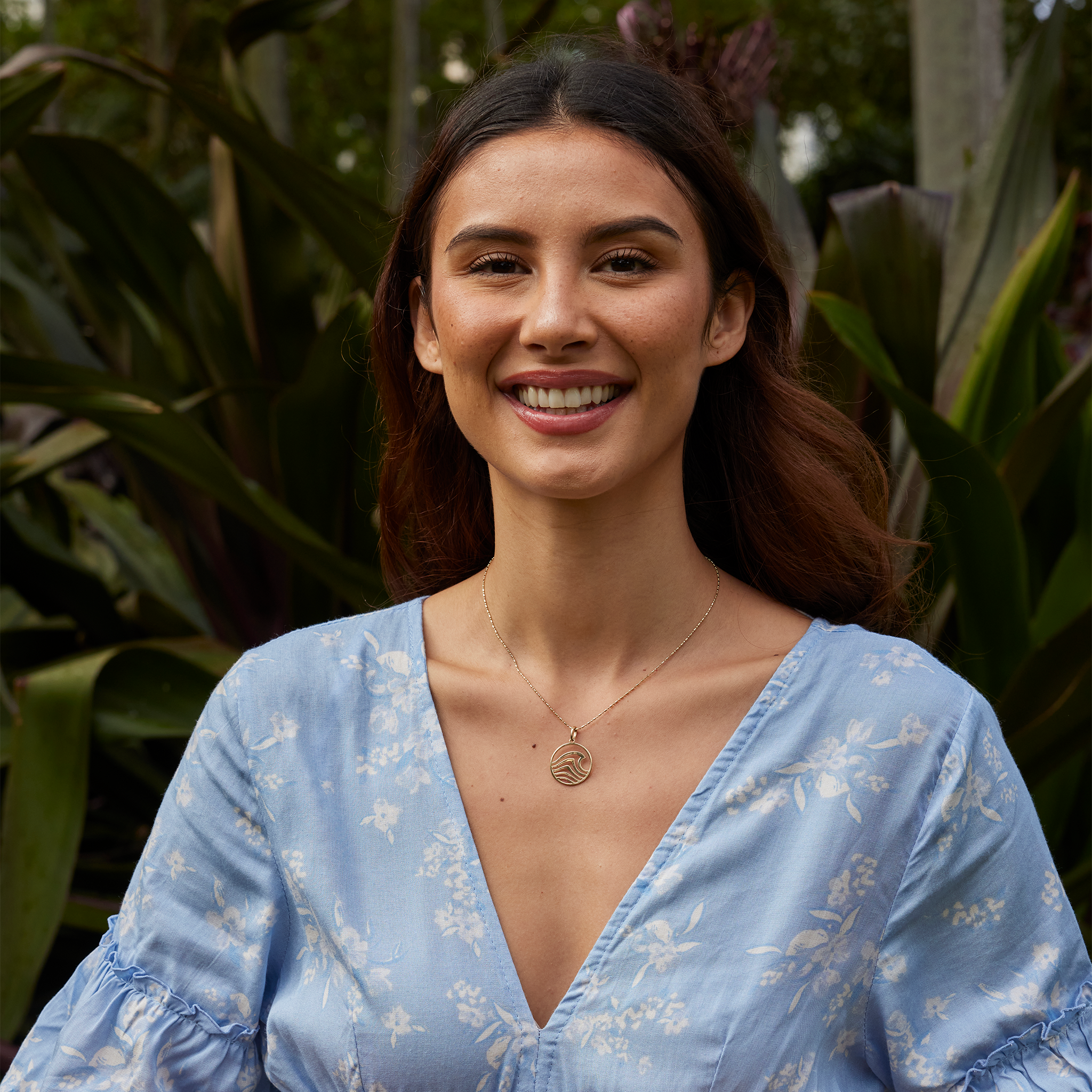 Woman in a lush garden wearing an abstract wave necklace in gold