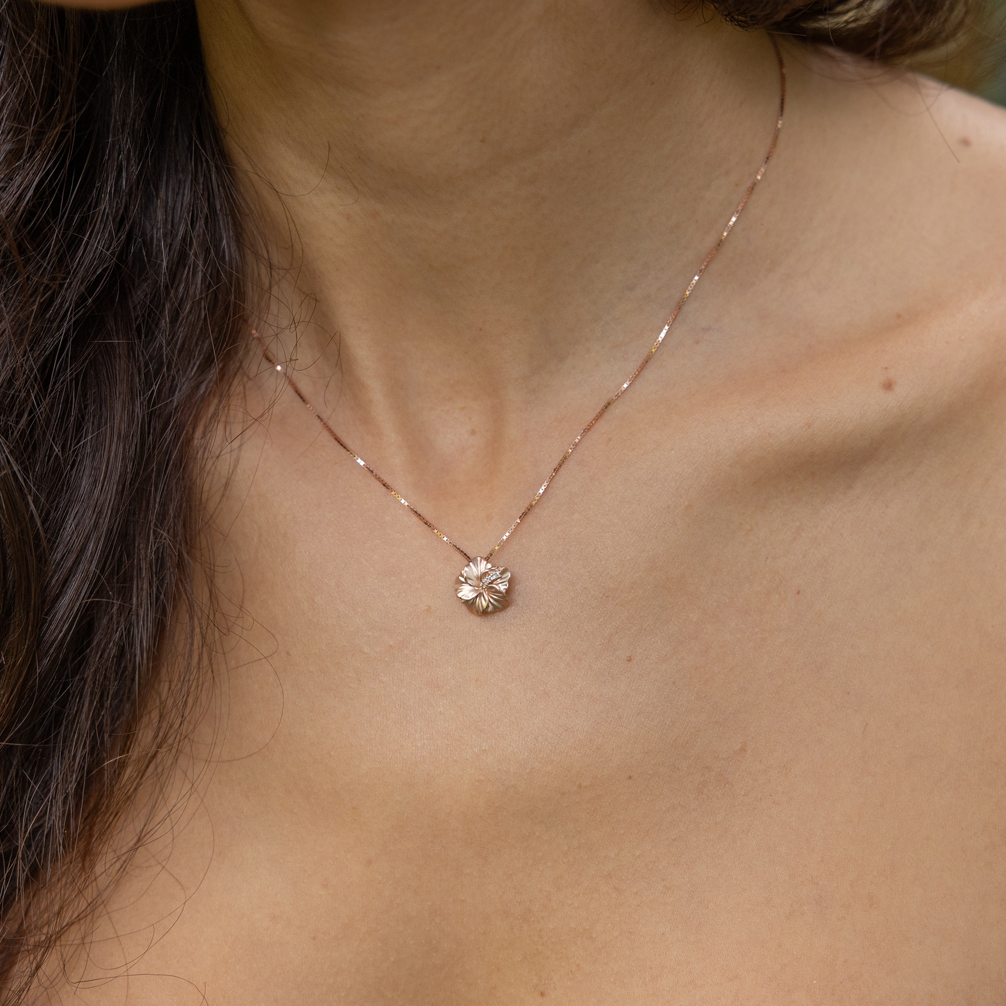 Person wearing the 11mm Diamond Hibiscus Pendant in 14k Rose Gold on a box chain