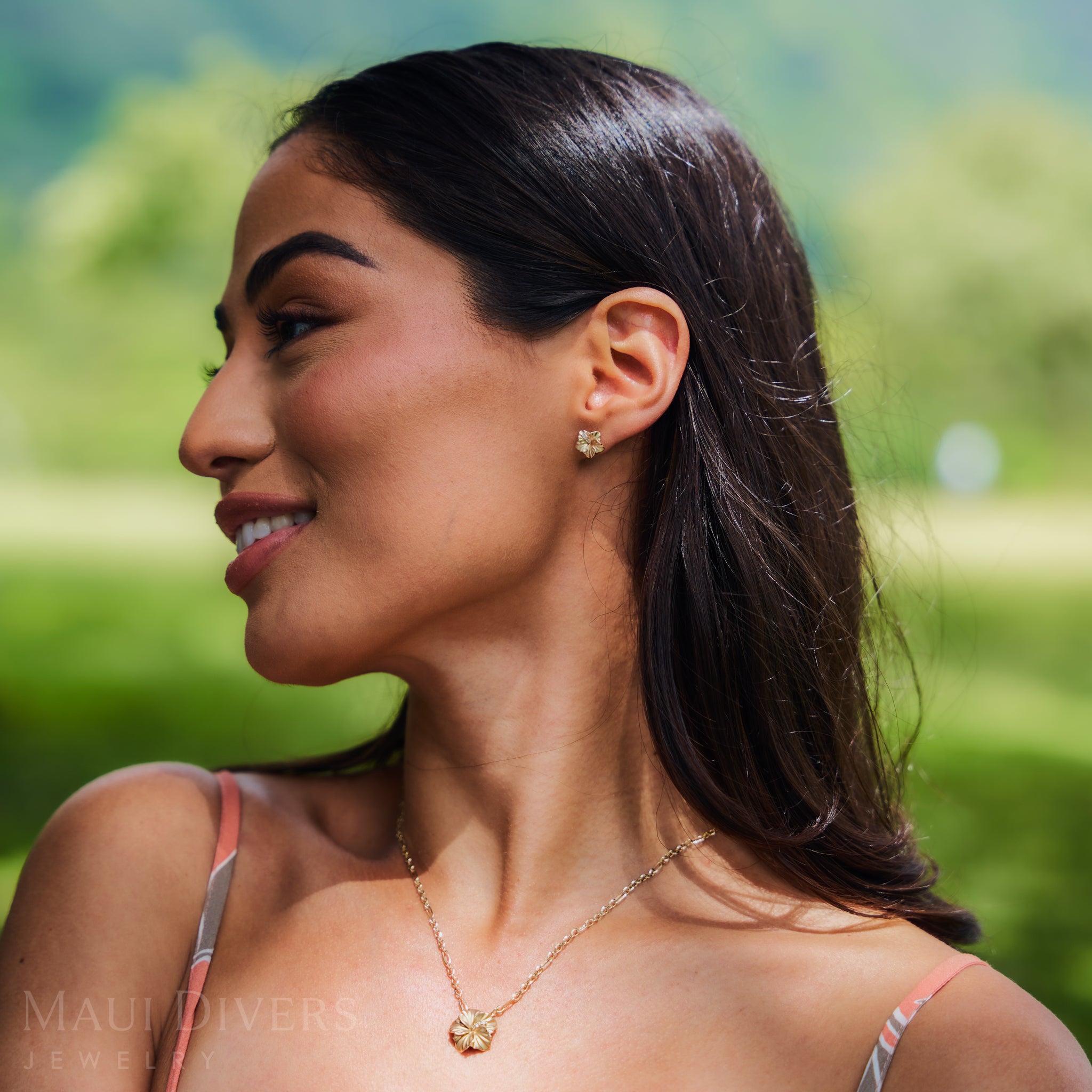 Close up of a woman in a garden wearing 9.5mm Diamond Hibiscus Earrings and Pendant in 14k Yellow Gold