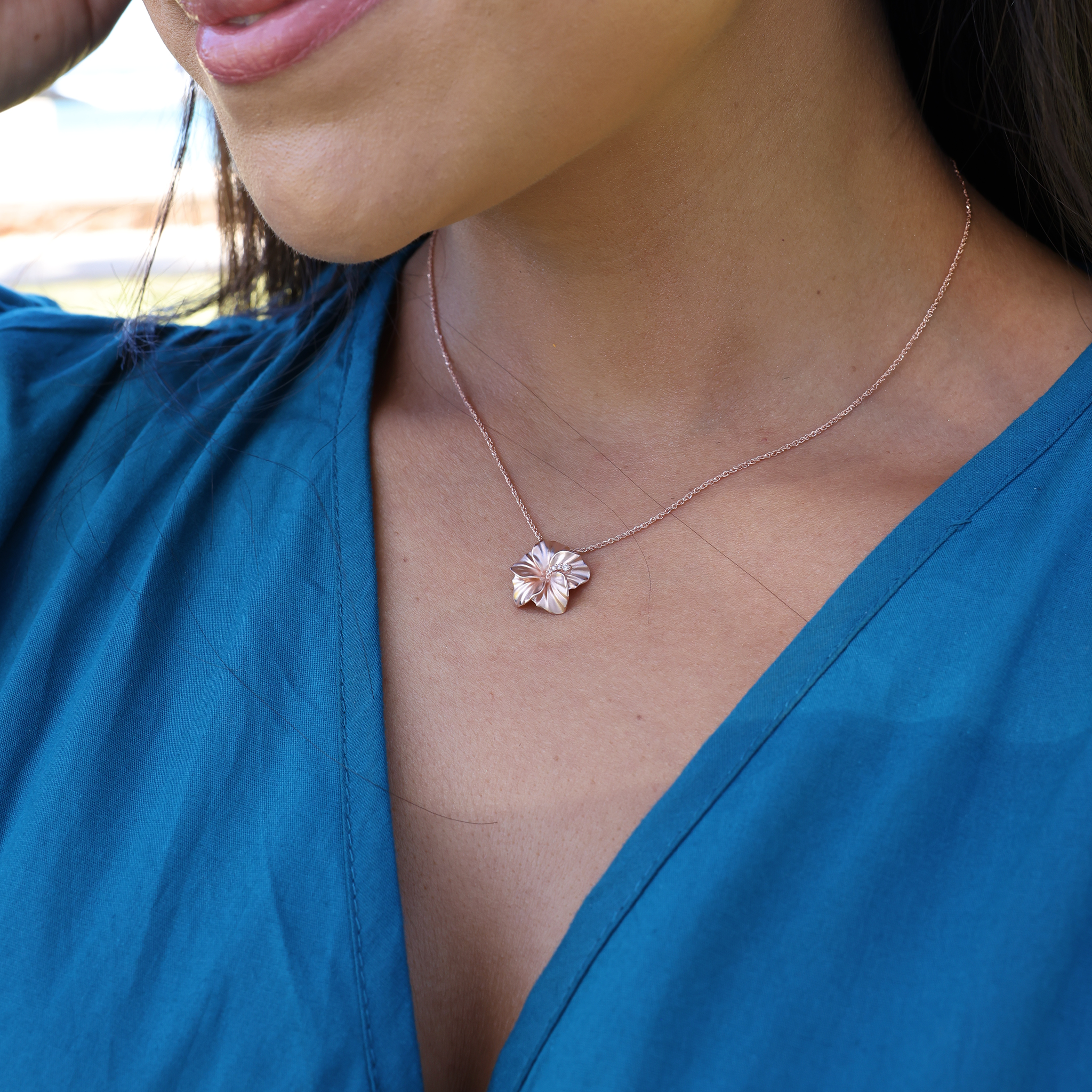Close up of a woman wearing a rose gold diamond hibiscus pendant on a rope chain