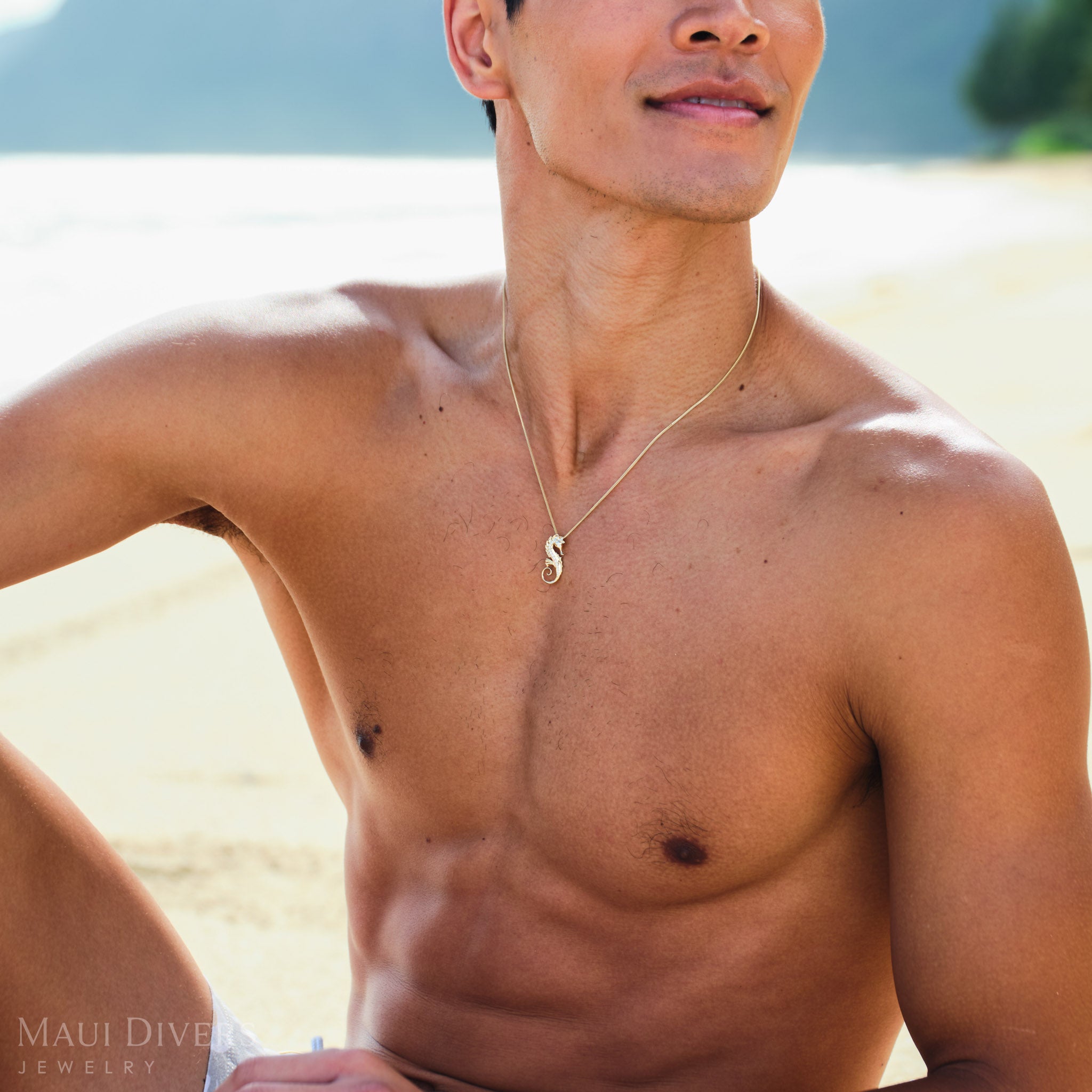 Man wearing a gold seahorse necklace with diamonds on a beach.
