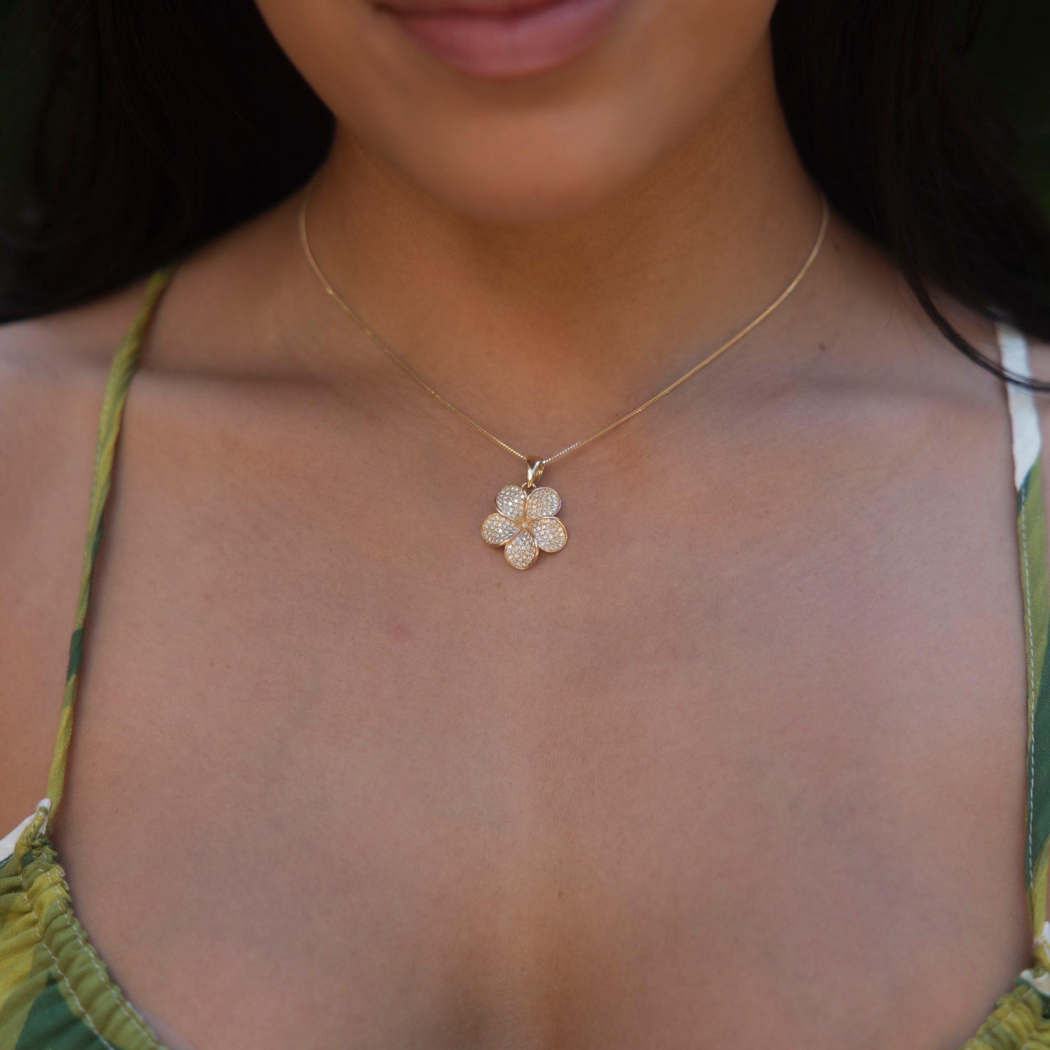 Woman's chest wearing Plumeria pendant in gold with pave set diamonds