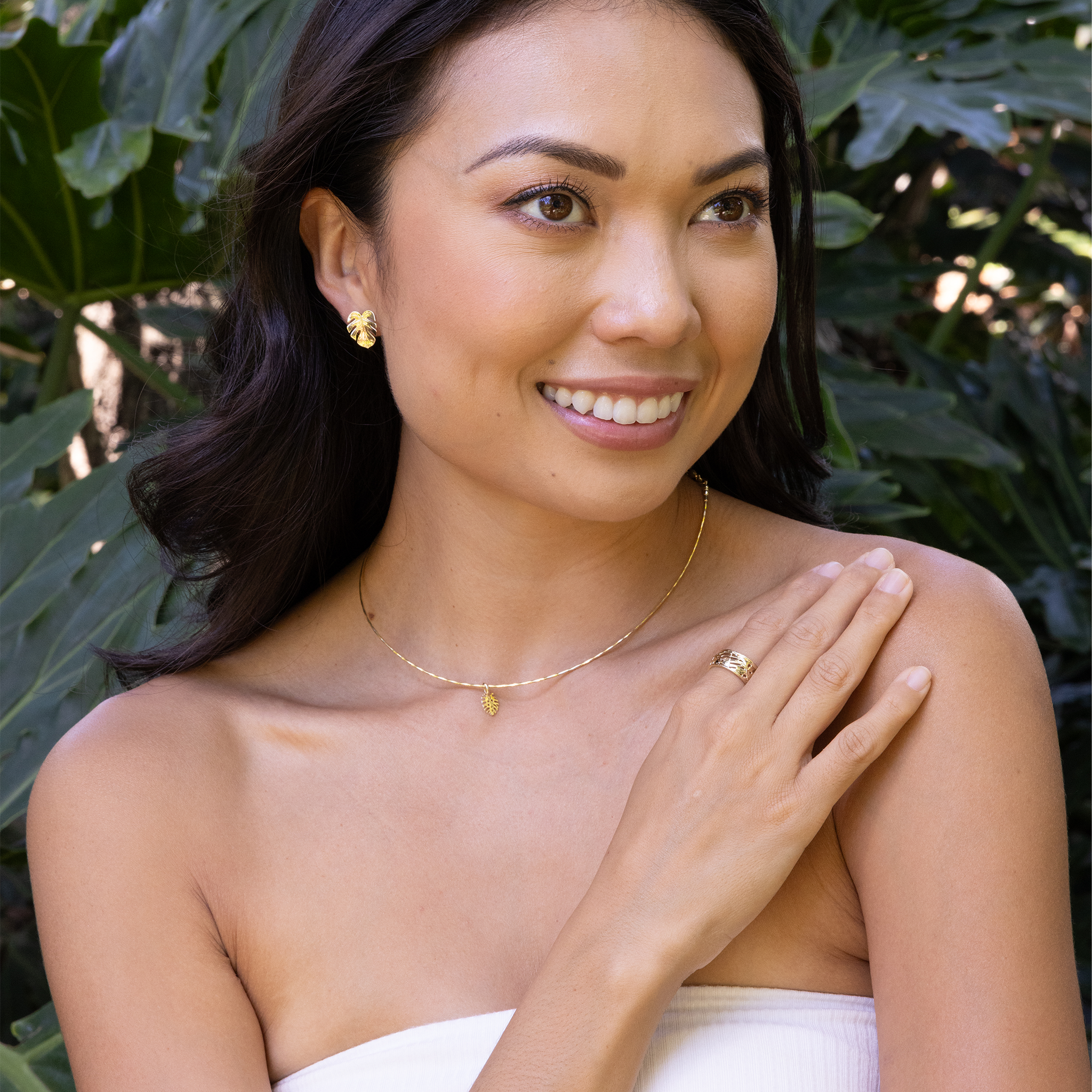 Woman in a tropical garden wearing Monstera Earrings, Ring and Pendant in gold