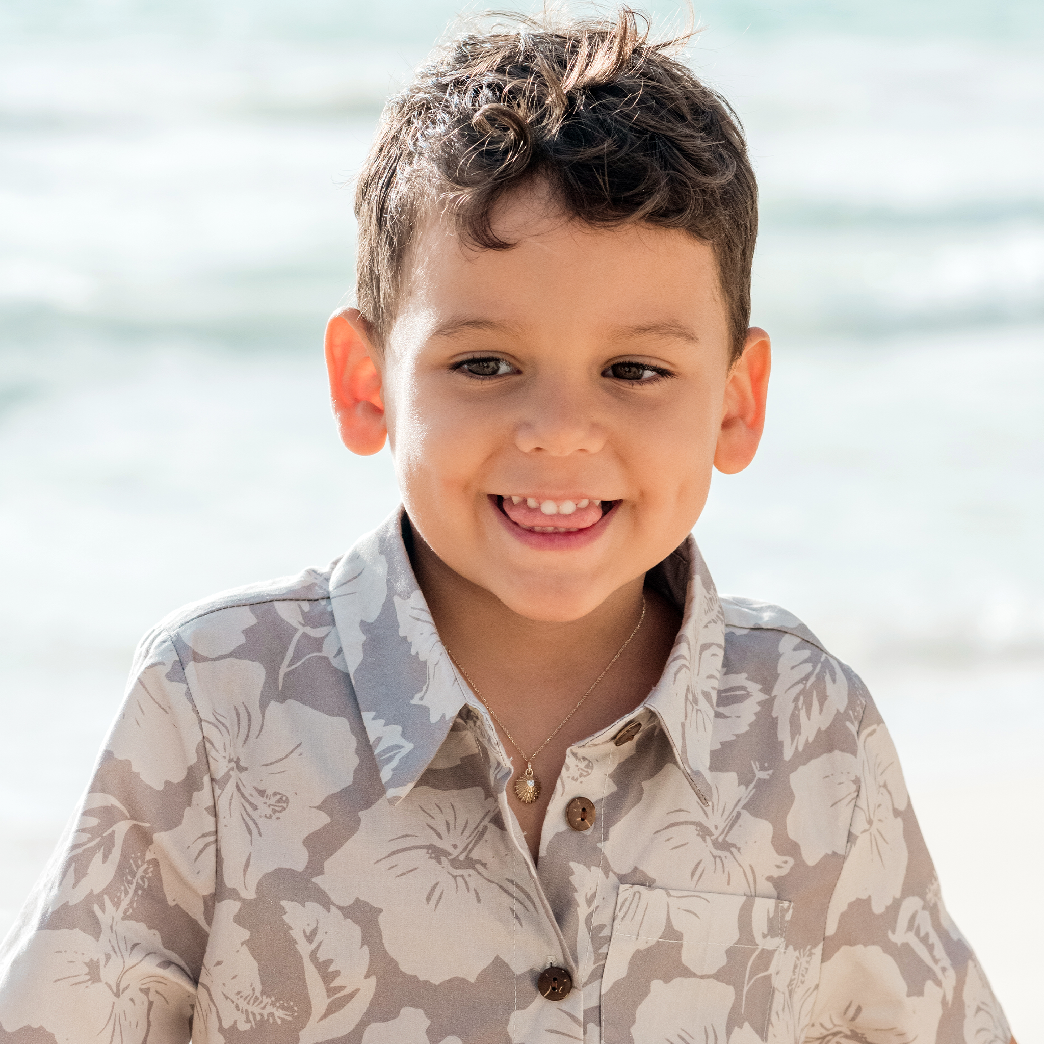 Boy wearing a gold necklace with an ʻOpihi diamond pendant against a blurred ocean background