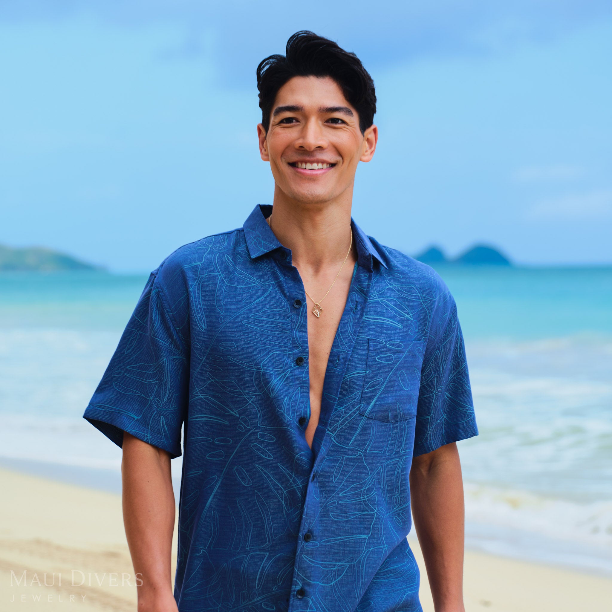 Man wearing a Koʻolau Mountain Necklace and blue patterned shirt on a beach