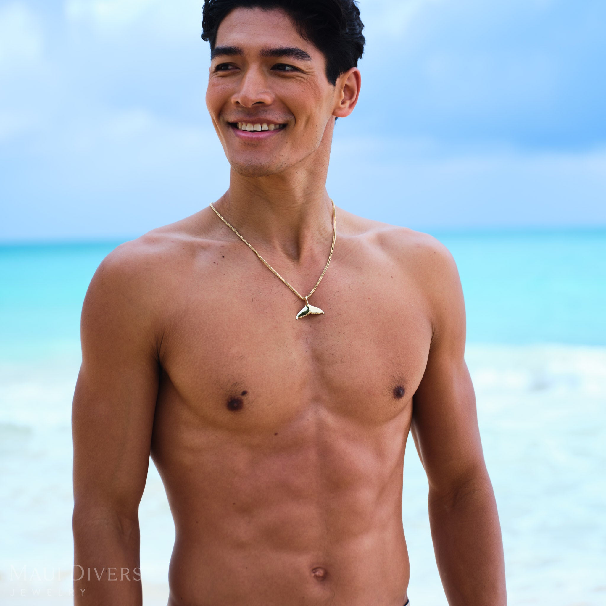 Man standing on a beach wearing a whale tail pendant with clear blue water and sky