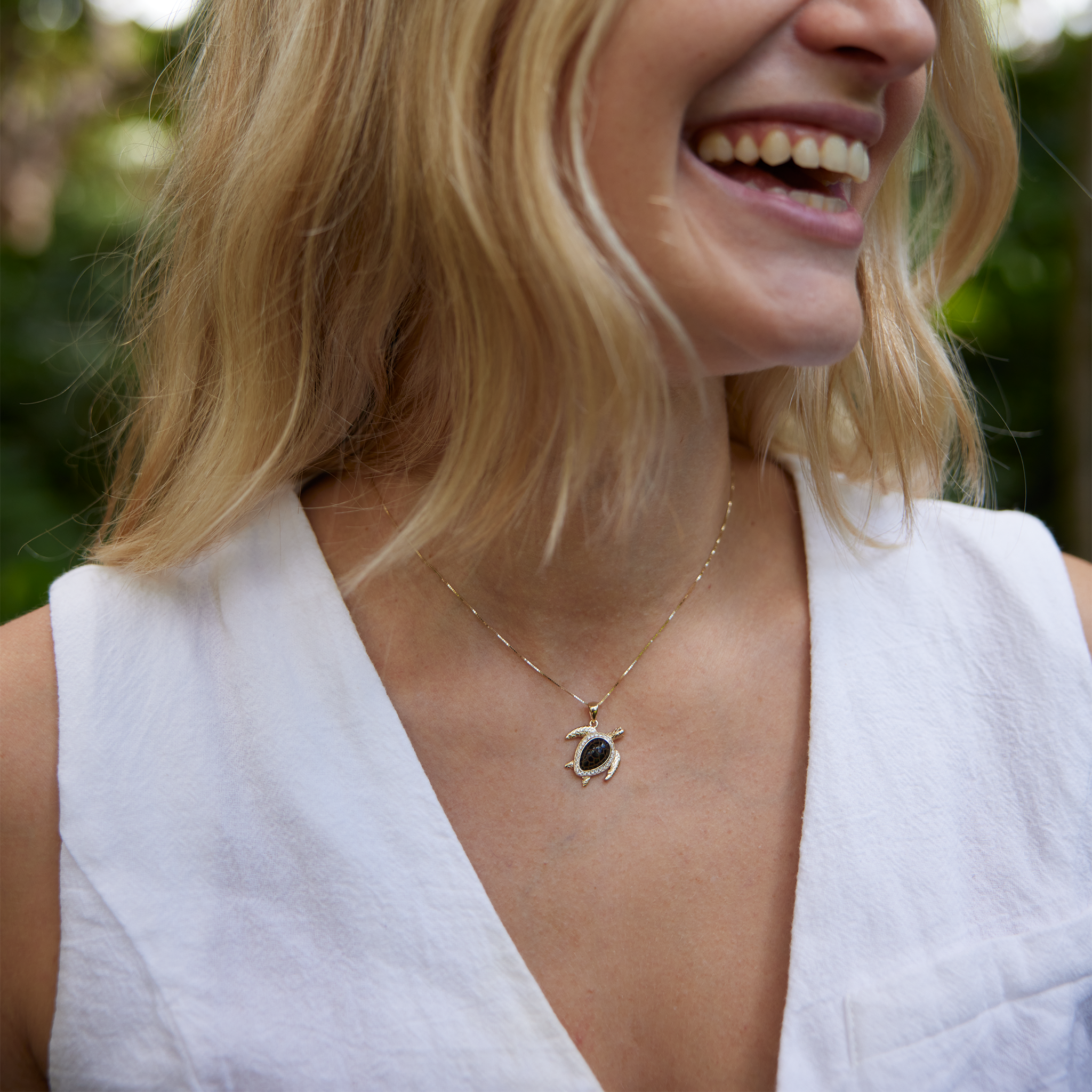 Woman with white shirt laughing and wearing Honu Black Coral Pendant in Gold with Diamonds - 18mm
