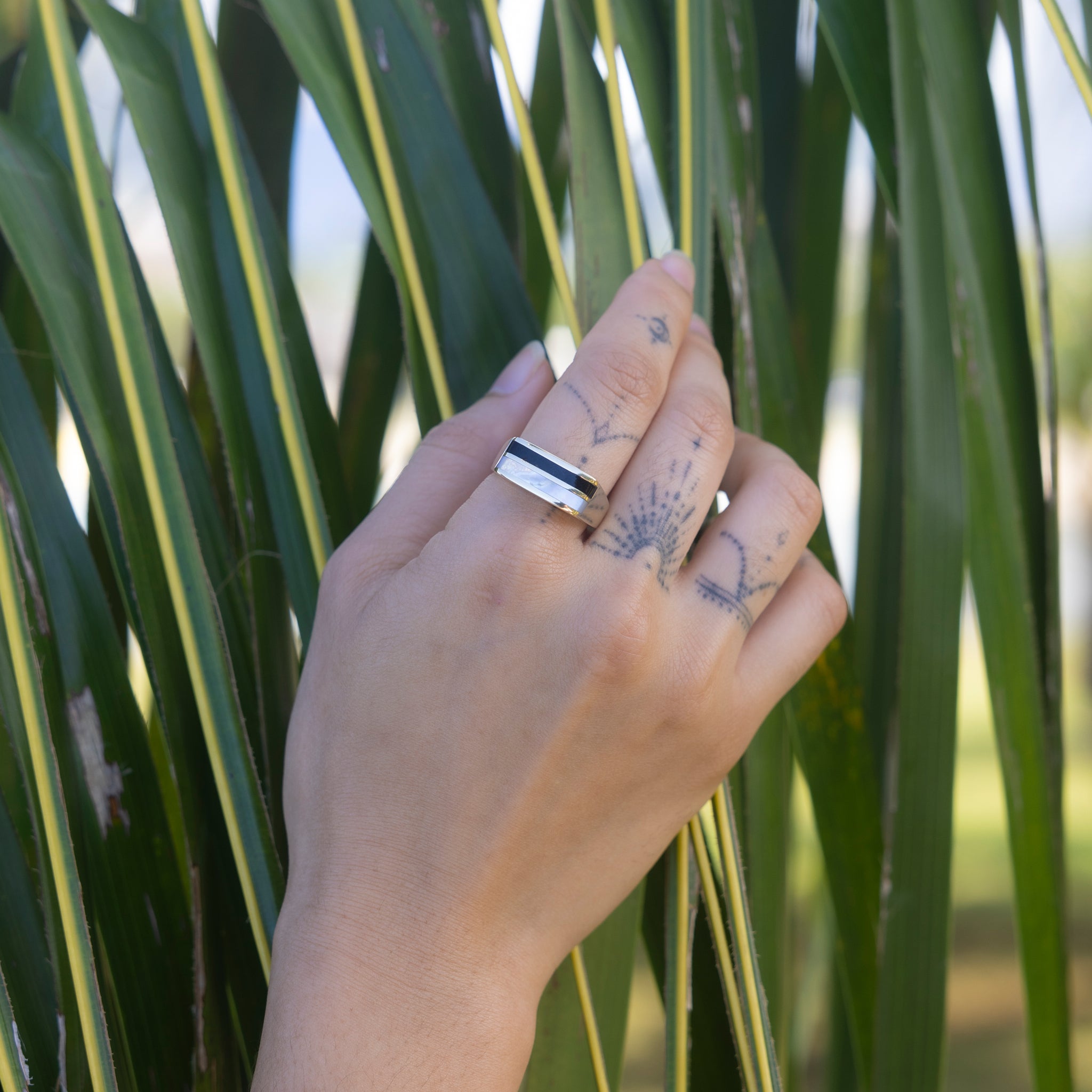 Hand holding palm leaf wearing Black Coral Ring in Gold with Mother of Pearl