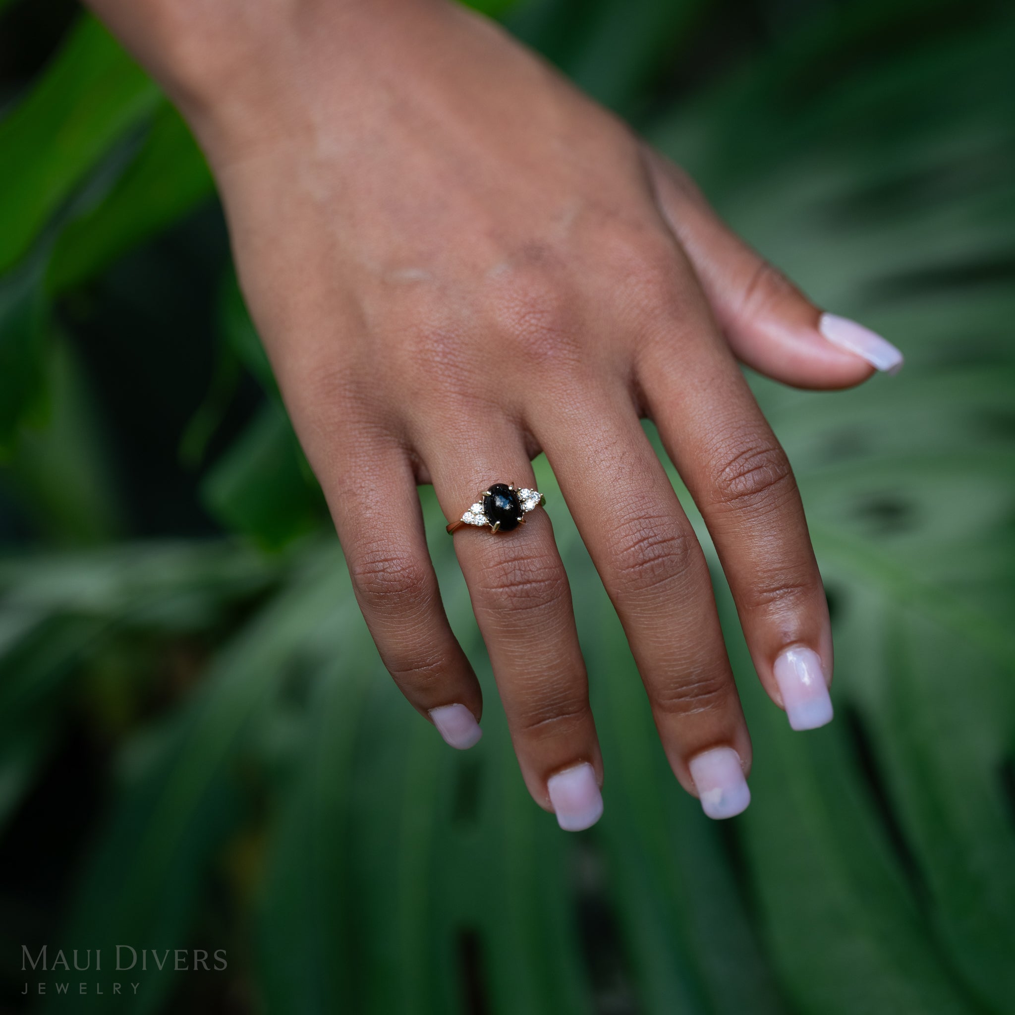 Hand wearing Black Coral Ring in Gold with Diamonds against monstera leaf background