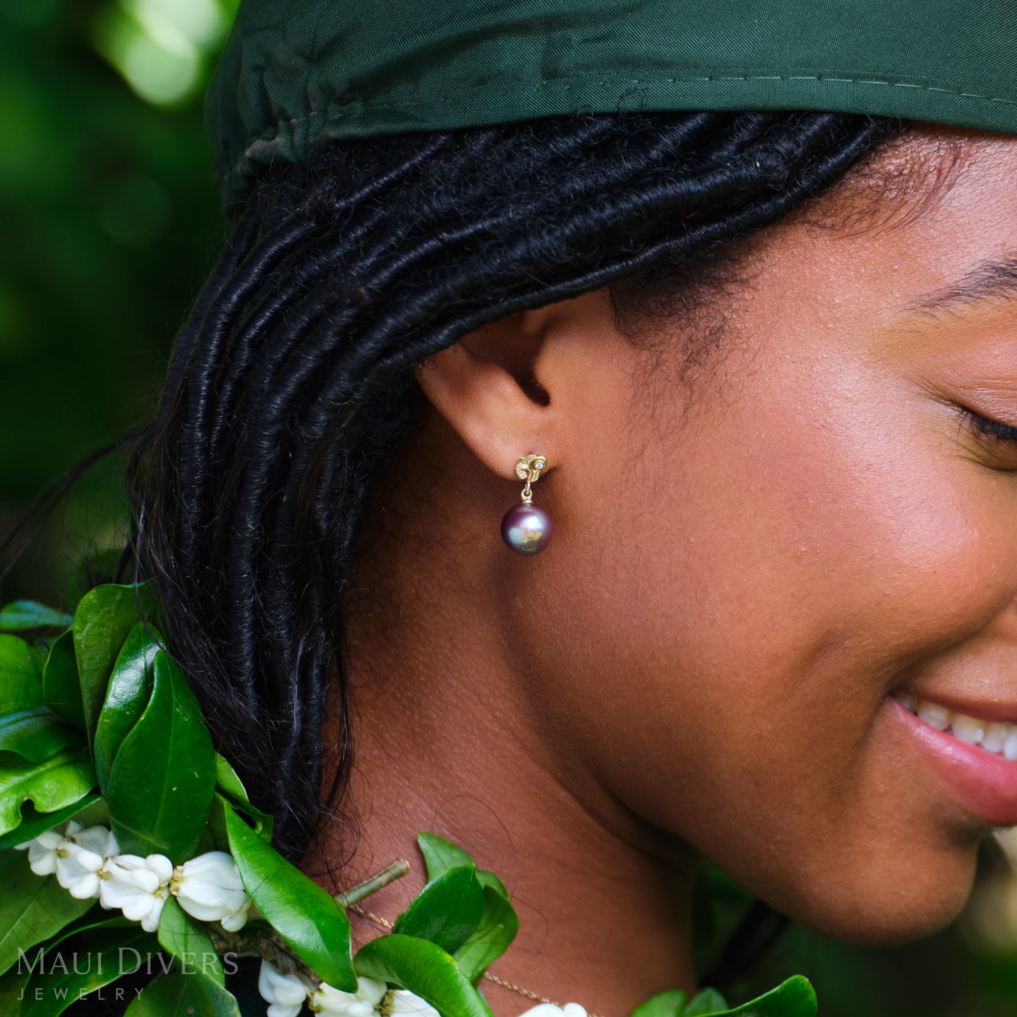 Close-up side view of a smiling woman wearing a Living Heirloom Freshwater Pearl Earring in 14k yellow gold with diamond accents on her right ear, against a blurred green background