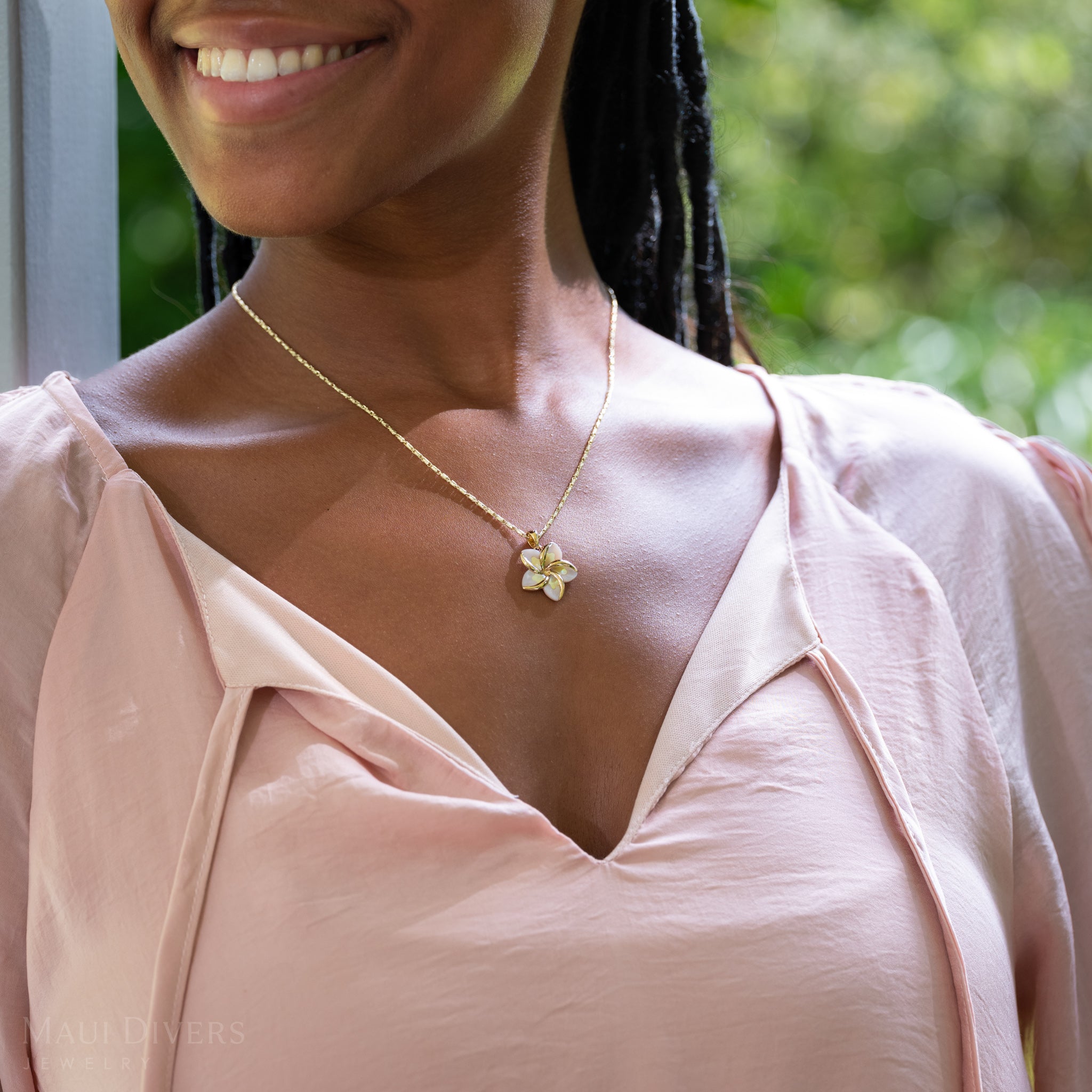 Close up of Plumeria Mother of Pearl Pendant in 14k Yellow Gold on woman's chest outdoors
