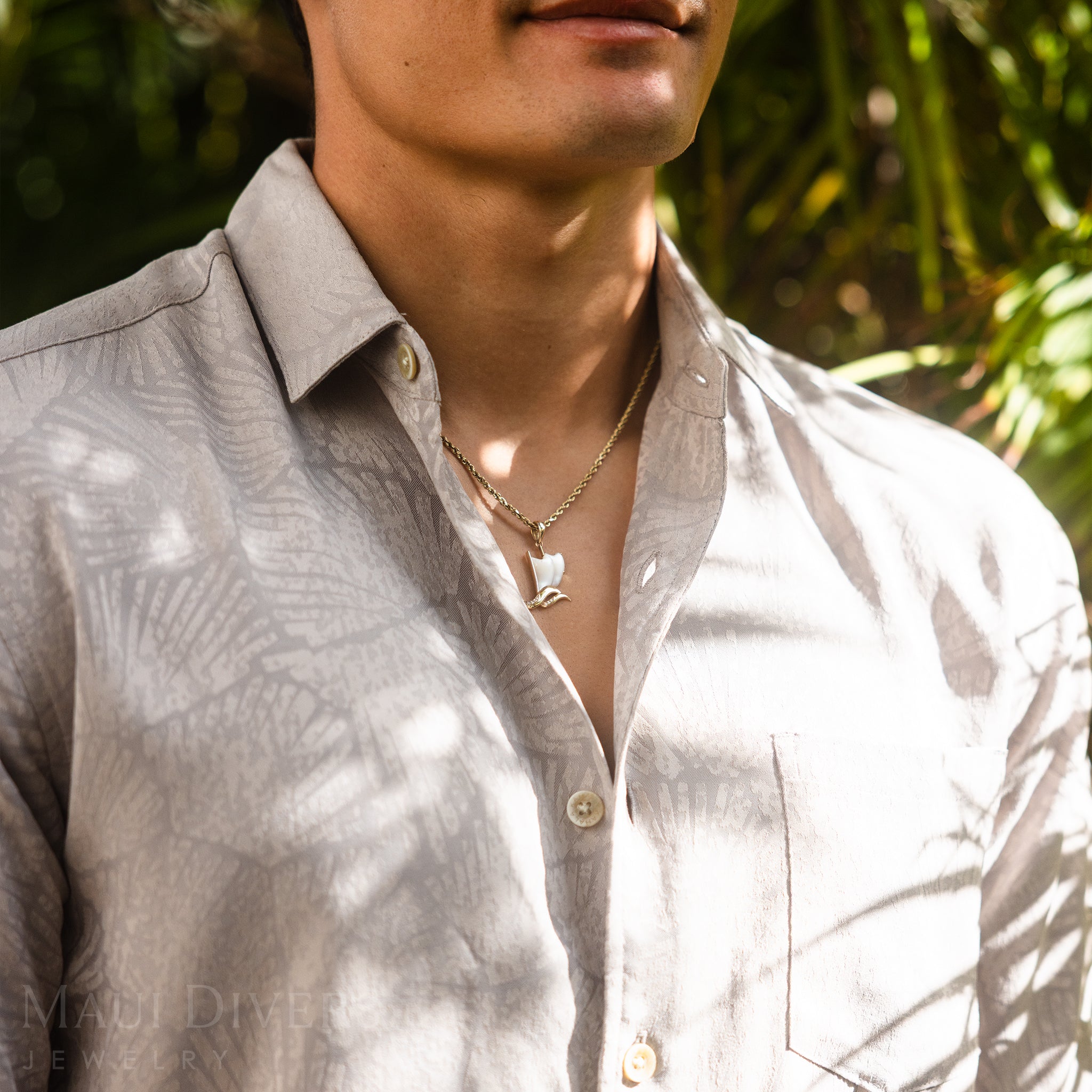 Person wearing a gold Waʻa (Canoe) pendant light-colored shirt with a blurred natural background
