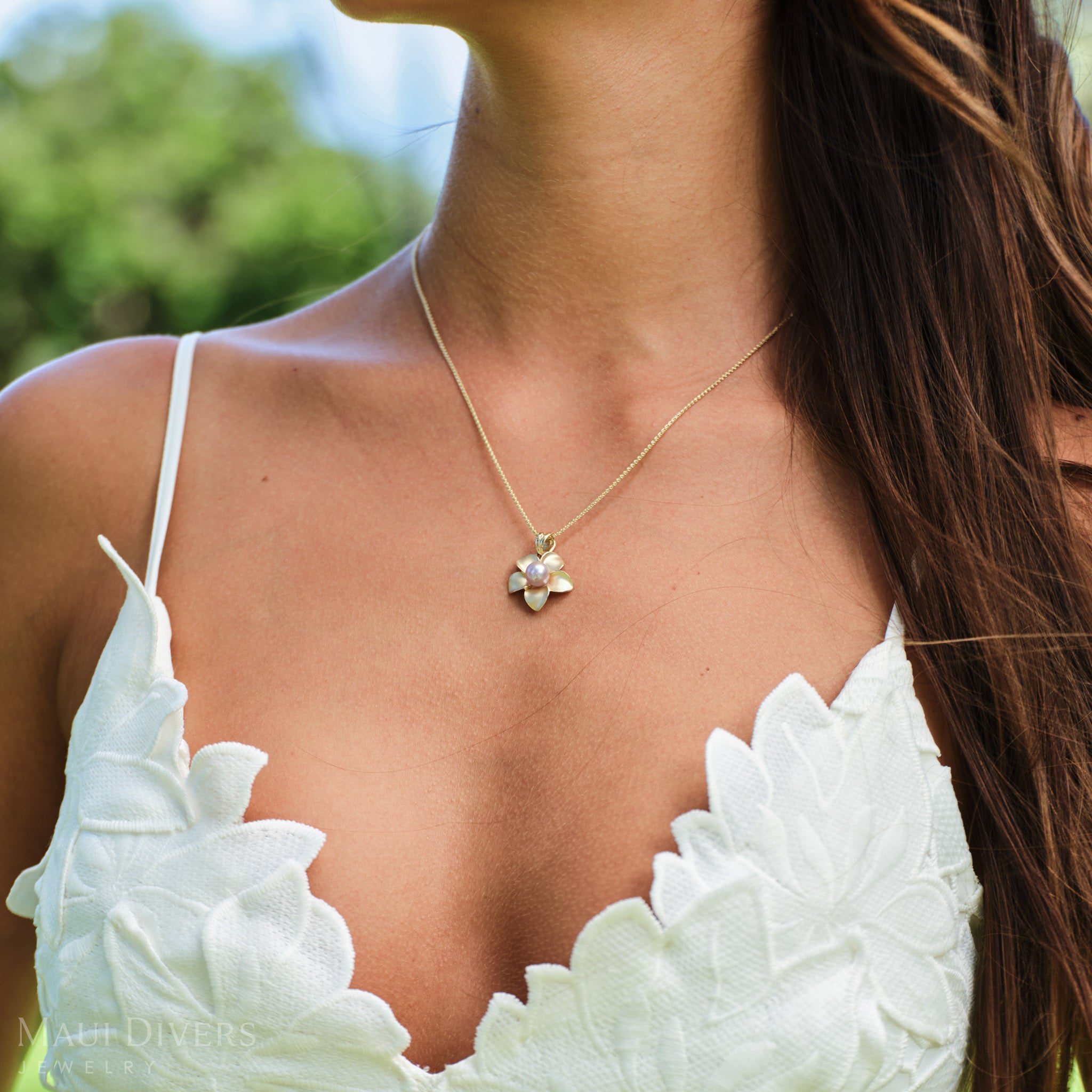 Close-up of an 18mm Pick A Pearl Plumeria Pendant in 14k yellow gold with a pink pearl worn around a neck
