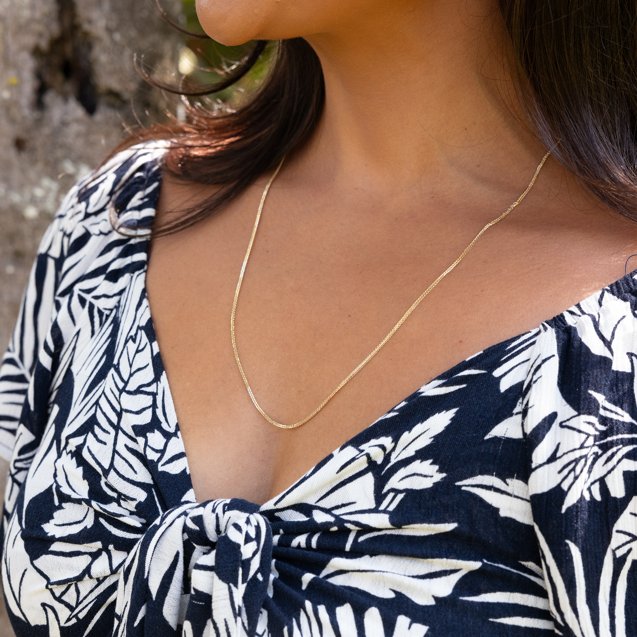 Close up of 1.4mm Espiga Chain in Gold on a woman wearing a black and white top