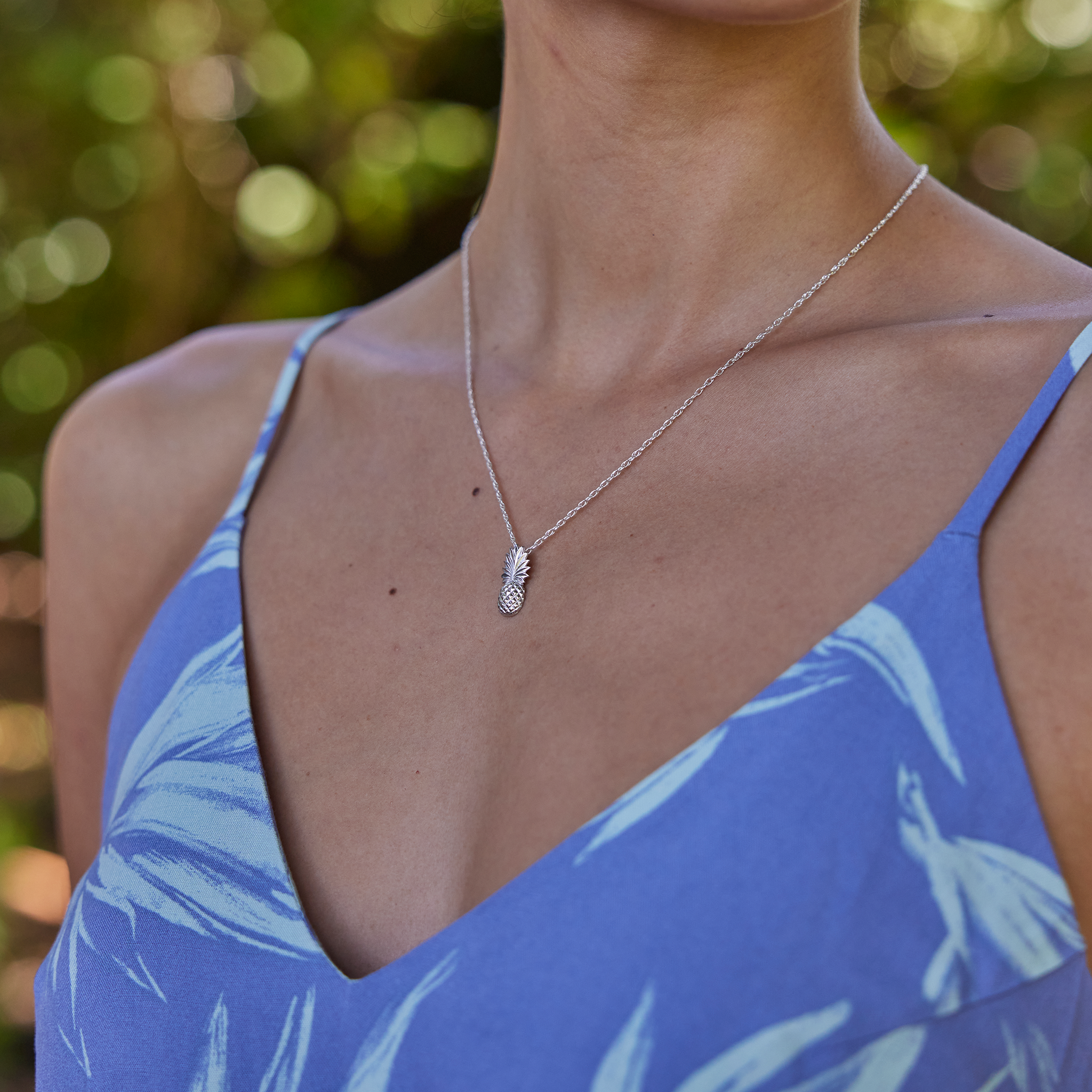 Close up of a Pineapple Pendant Necklace in Sterling Silver on a woman's chest with blurred green background