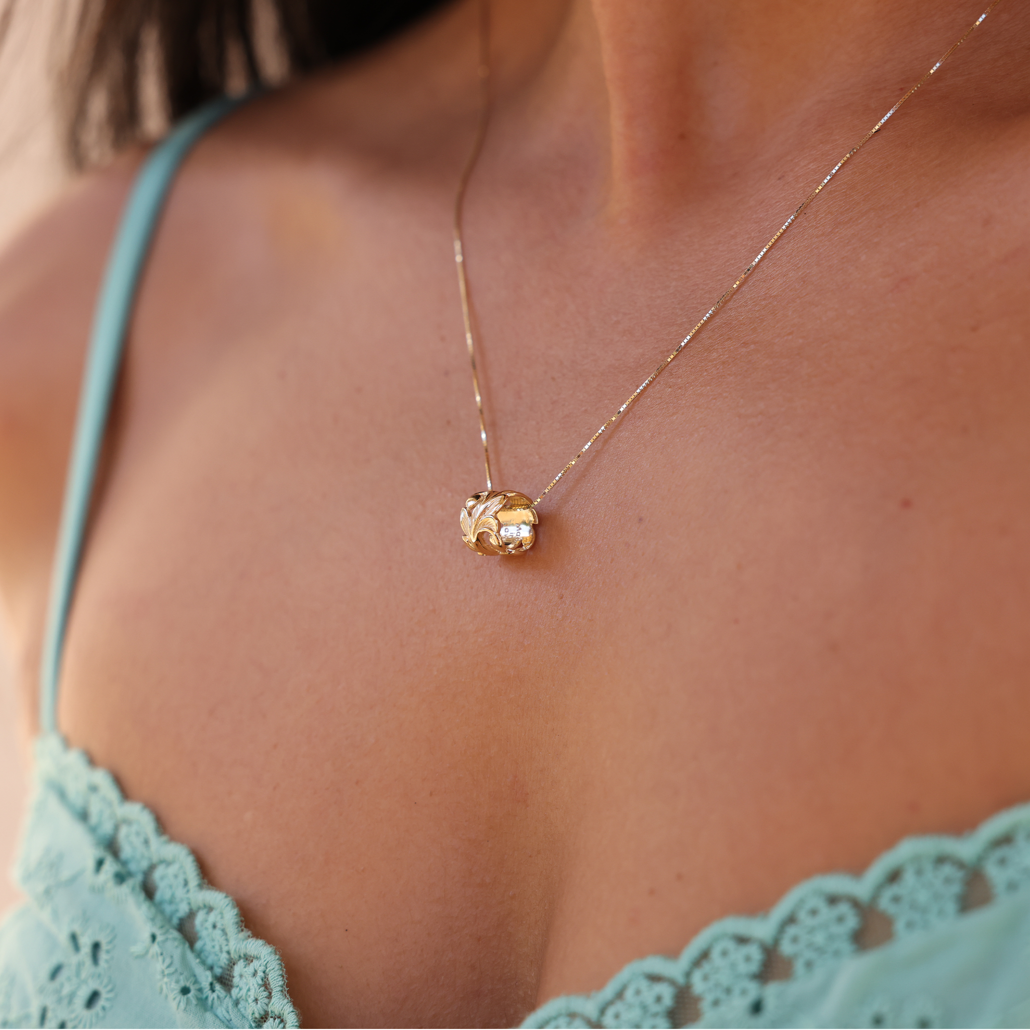 Hawaiian Heirloom Maile Scroll Barrel Pendant in Gold on Woman's Chest with Teal Top