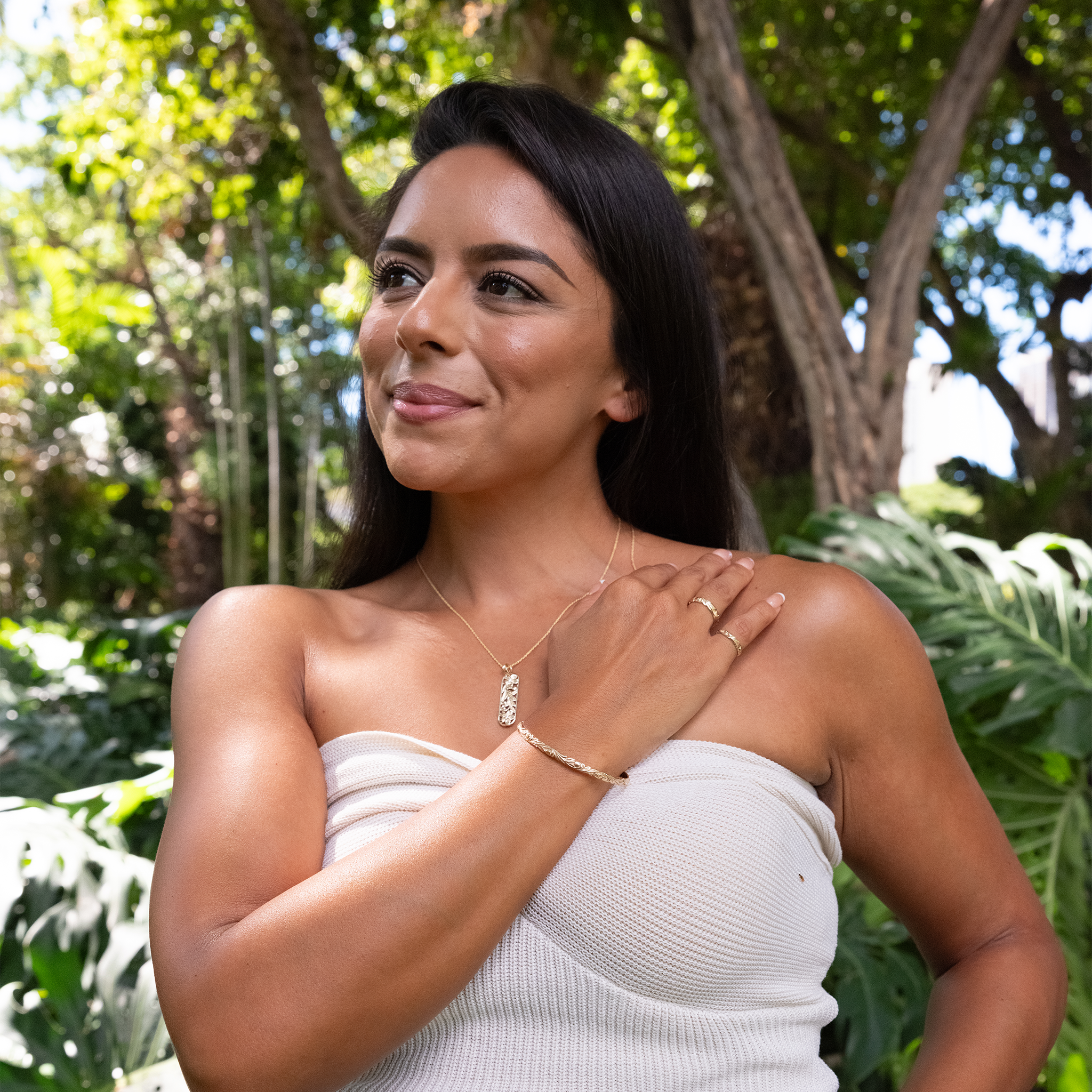 Woman in a garden wearing a Hawaiian Heirloom Old English Scroll Bracelet in Gold