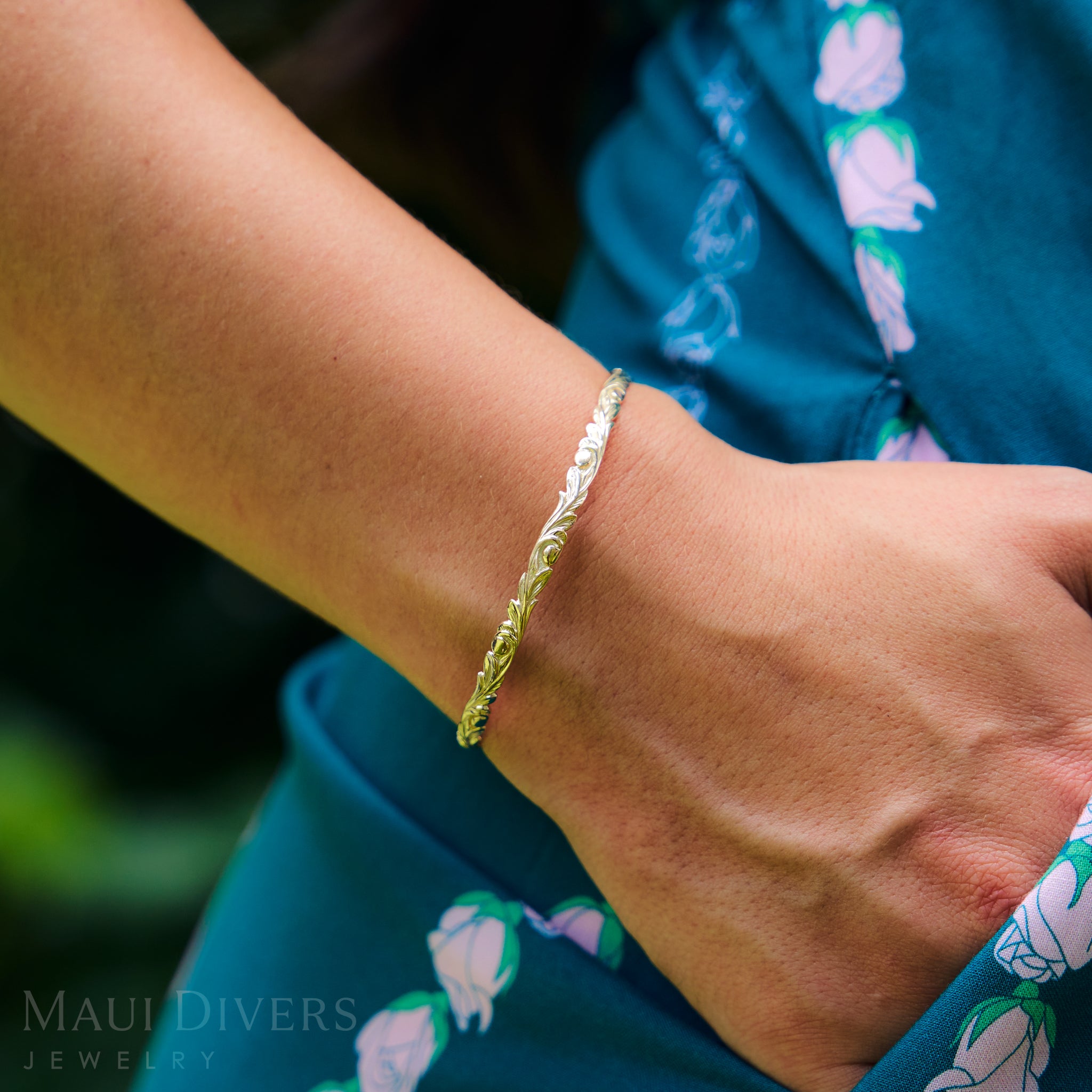 Hawaiian Heirloom Old English Scroll Bracelet in Gold on a wrist with a blurred background