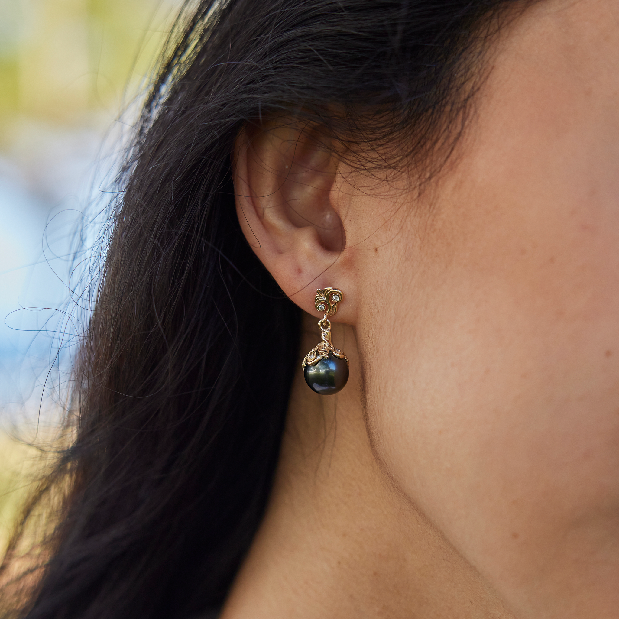 Woman's right ear wearing a Living Heirloom Tahitian Black Pearl Earrings in Gold with Diamonds outdoors