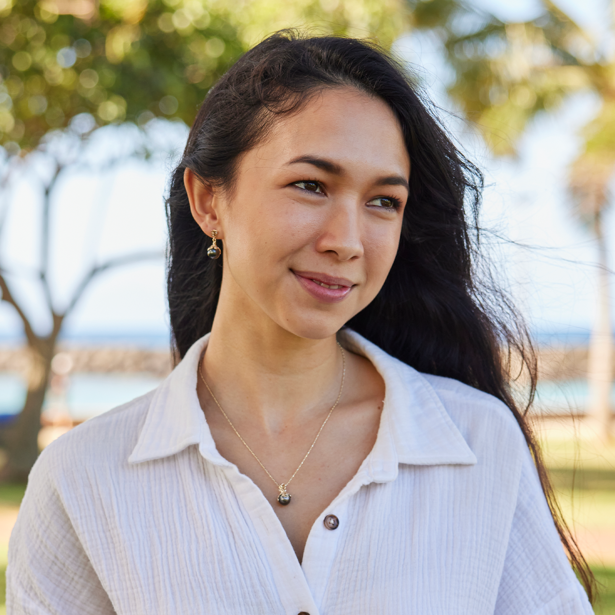 Woman in a beach park wearing a Living Heirloom Tahitian Black Pearl Earrings in Gold with Diamonds