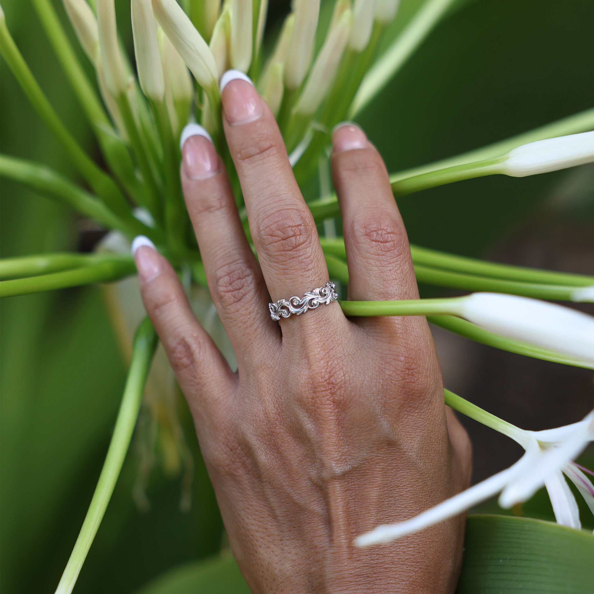 Woman's hand with Living Heirloom Ring in White Gold with Diamonds against a white flower plant