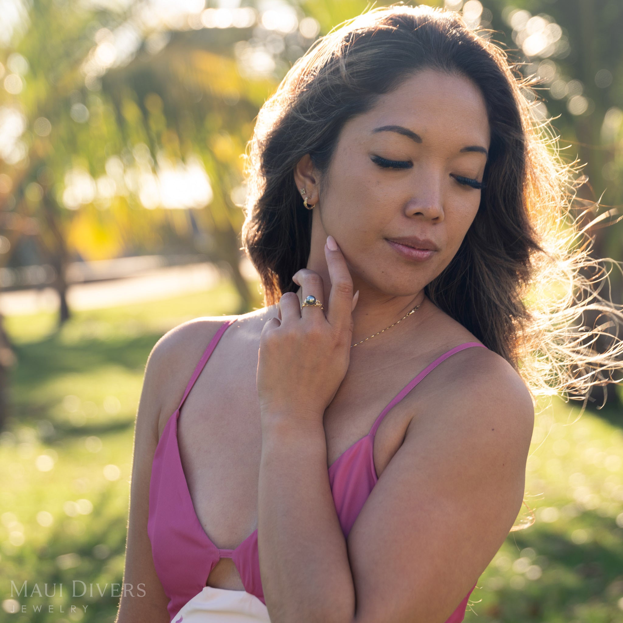 Woman in a pink dress wearing a Tahitian black pearl ring in 14k yellow gold outdoors with blurred greenery in the background